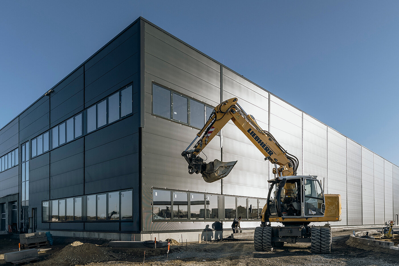 Neugebautes modernes Gebäude mit Baustellenfahrzeug im Vordergrund, unter blauem Himmel.