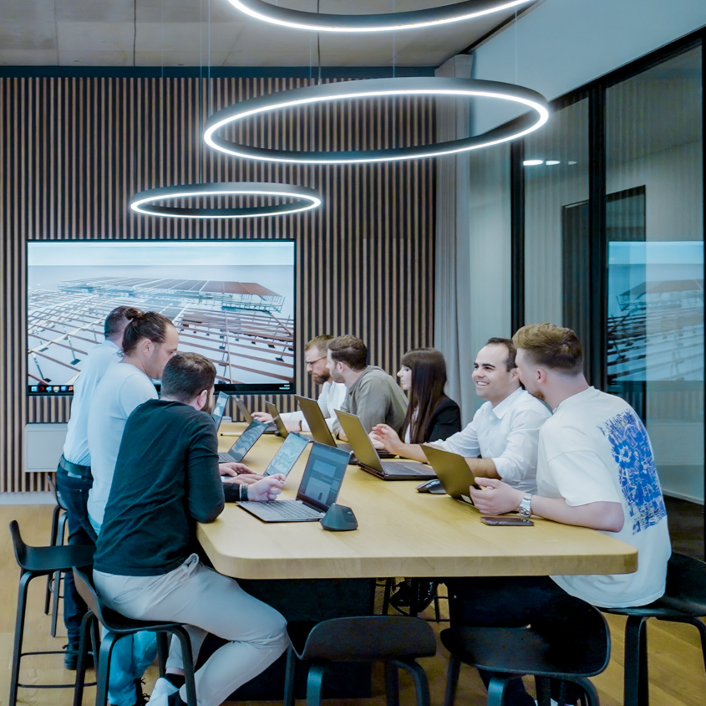 Gruppensitzung in modernem Besprechungsraum mit Laptopnutzung und Präsentation im Hintergrund.