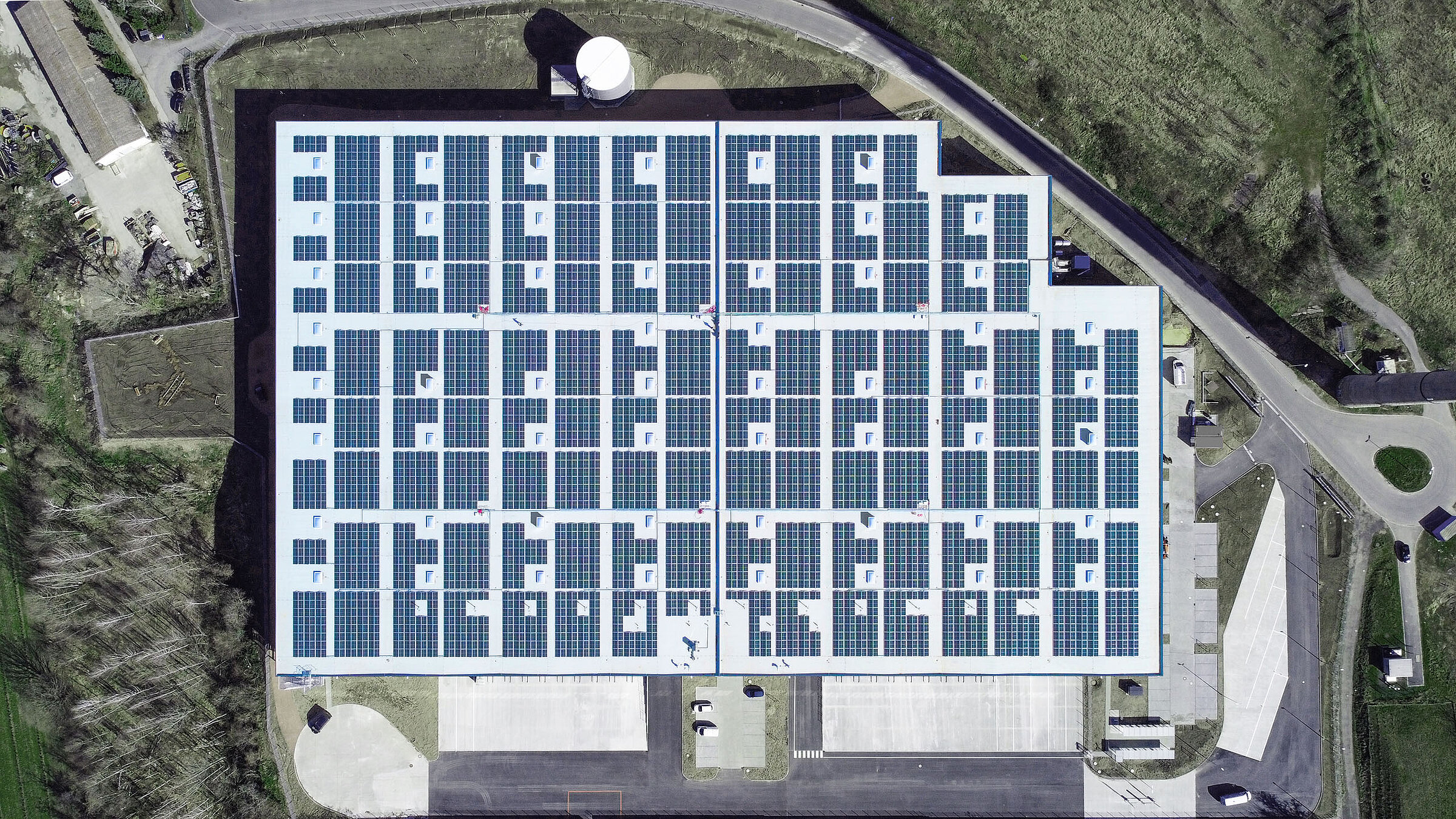 Dachansicht eines modernen Gebäudes mit Solarzellen auf dem Dach und angrenzenden Parkplätzen.
