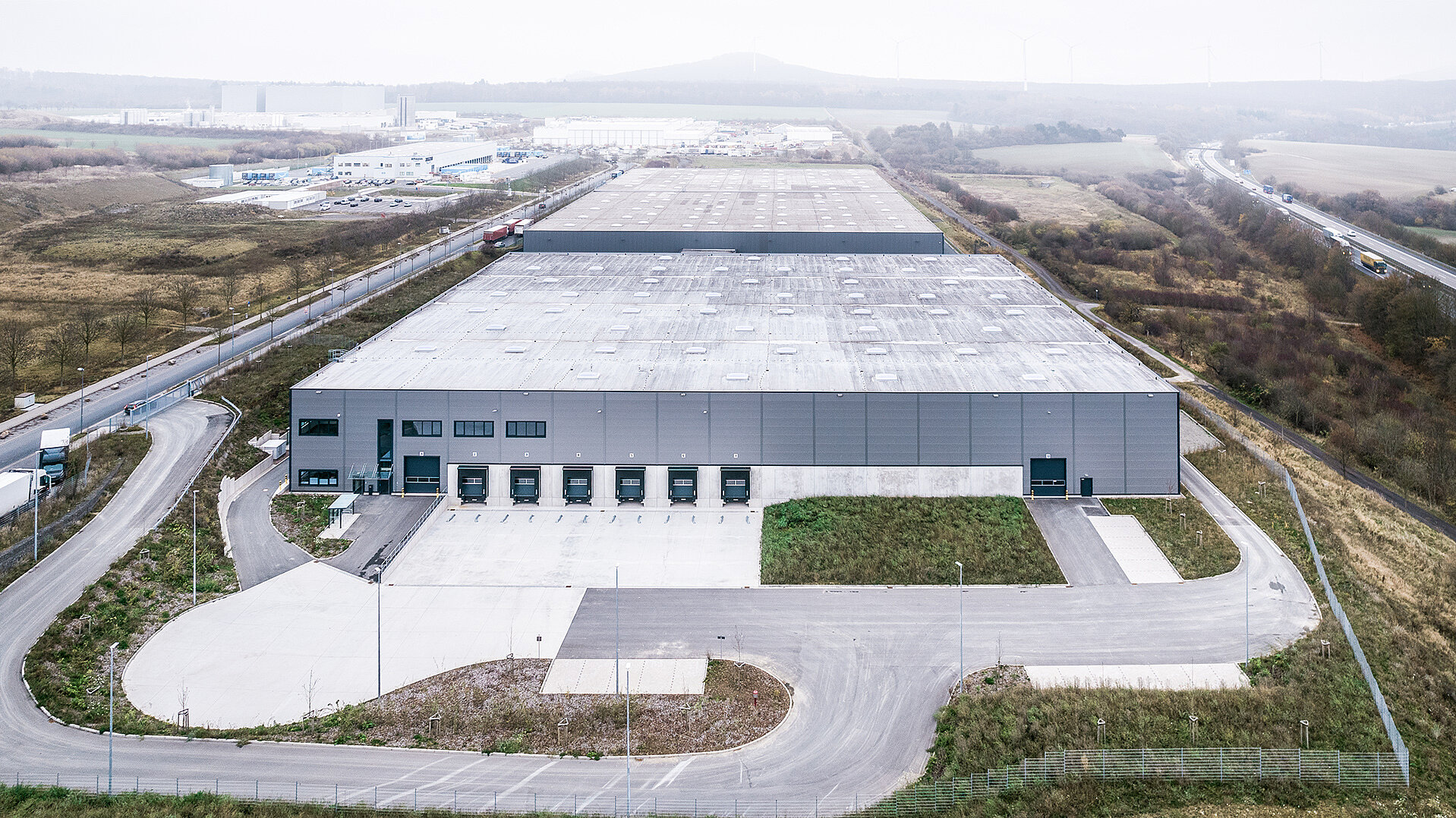 Luftaufnahme eines großen Lagerhauses mit umliegenden Straßen und einer grünen Landschaft im Hintergrund.