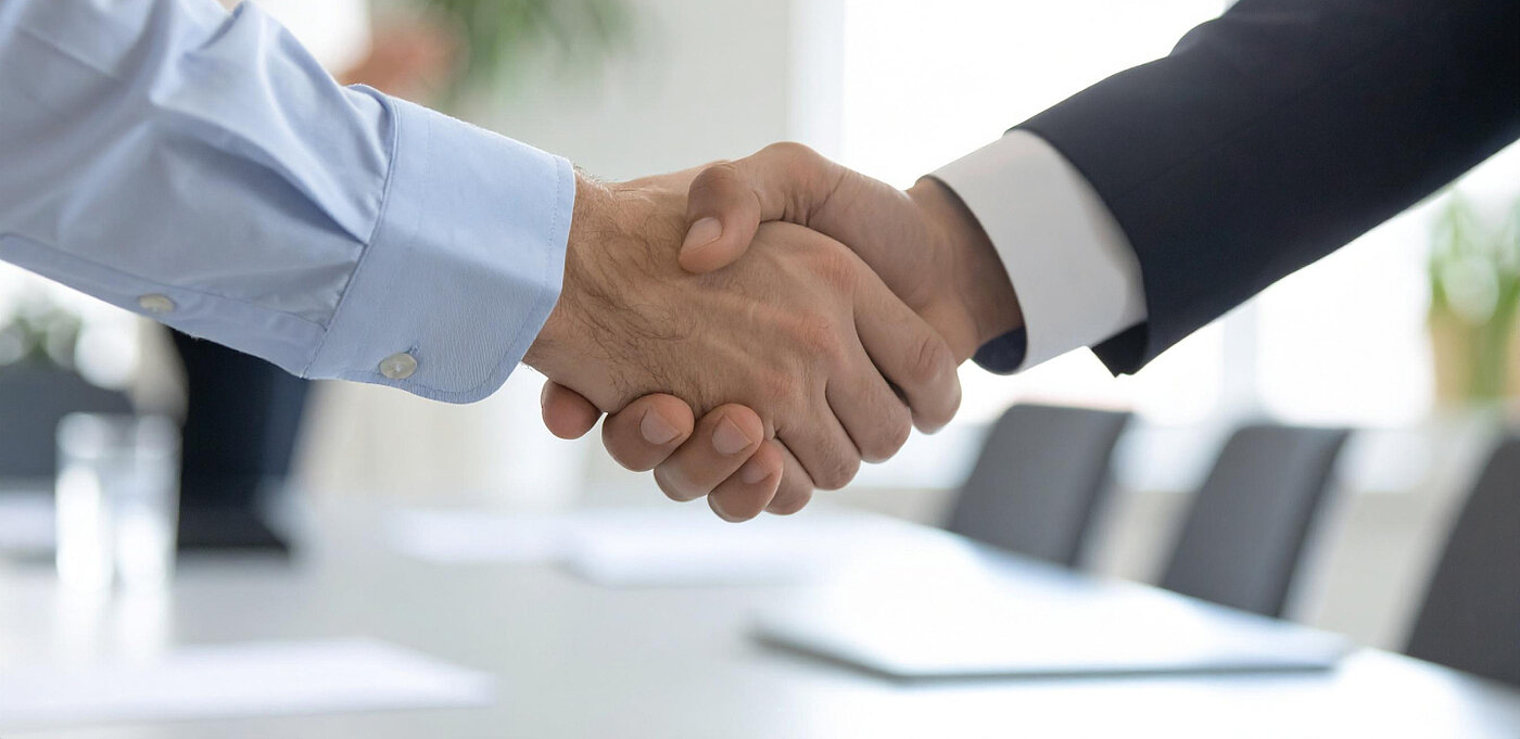 Zwei Personen schütteln sich die Hände in einem hellen Büroraum.