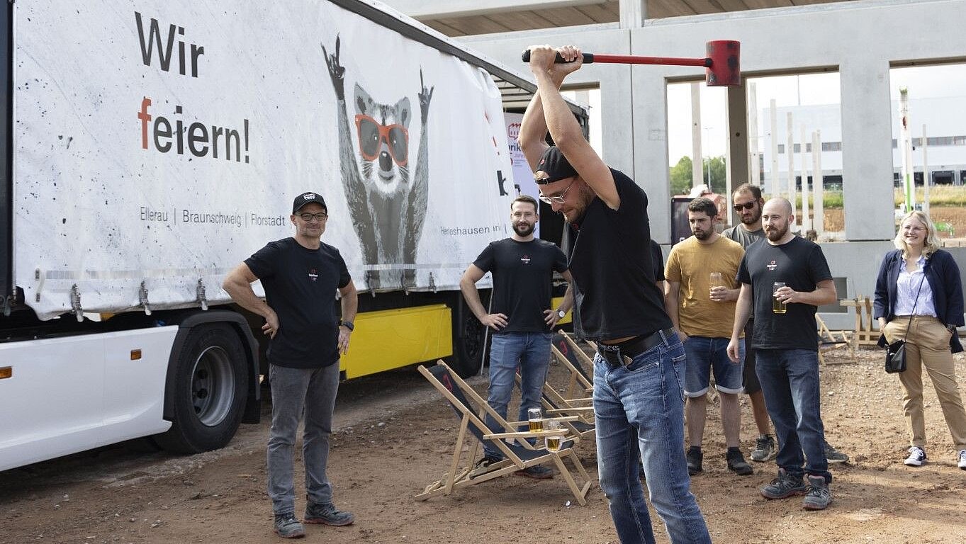 A group of people are celebrating on a construction site while one person raises a hammer to perform an action.