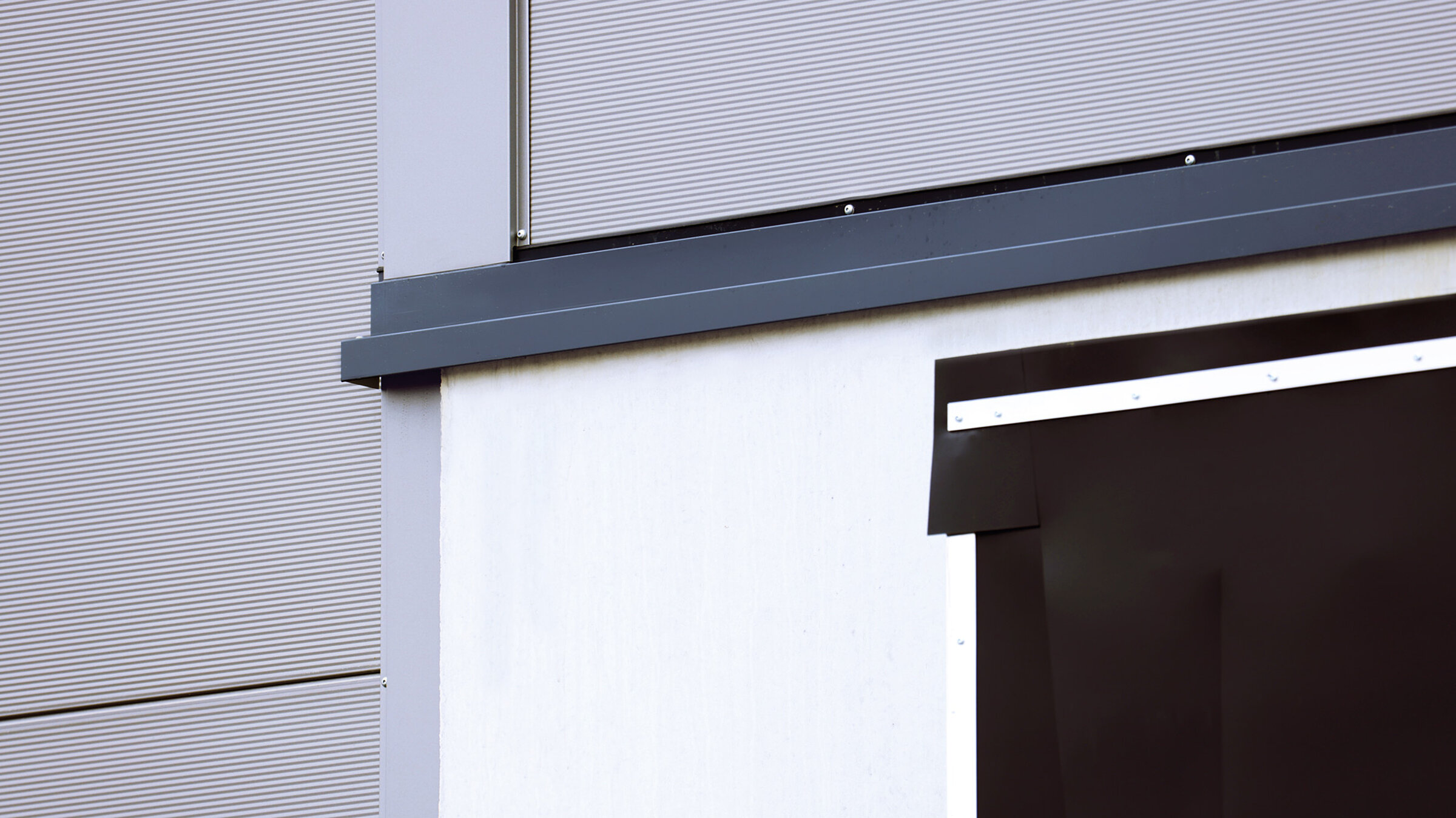 Detailansicht einer modernen Gebäudefassade mit glatten und strukturierten Oberflächen in Grautönen.