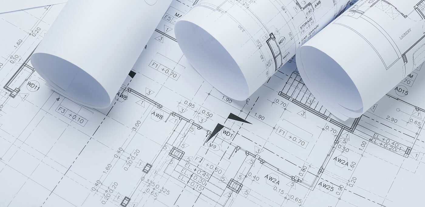 Rollende Baupläne auf einem technischen Zeichnungsblatt, das Maßstab und Details zeigt.