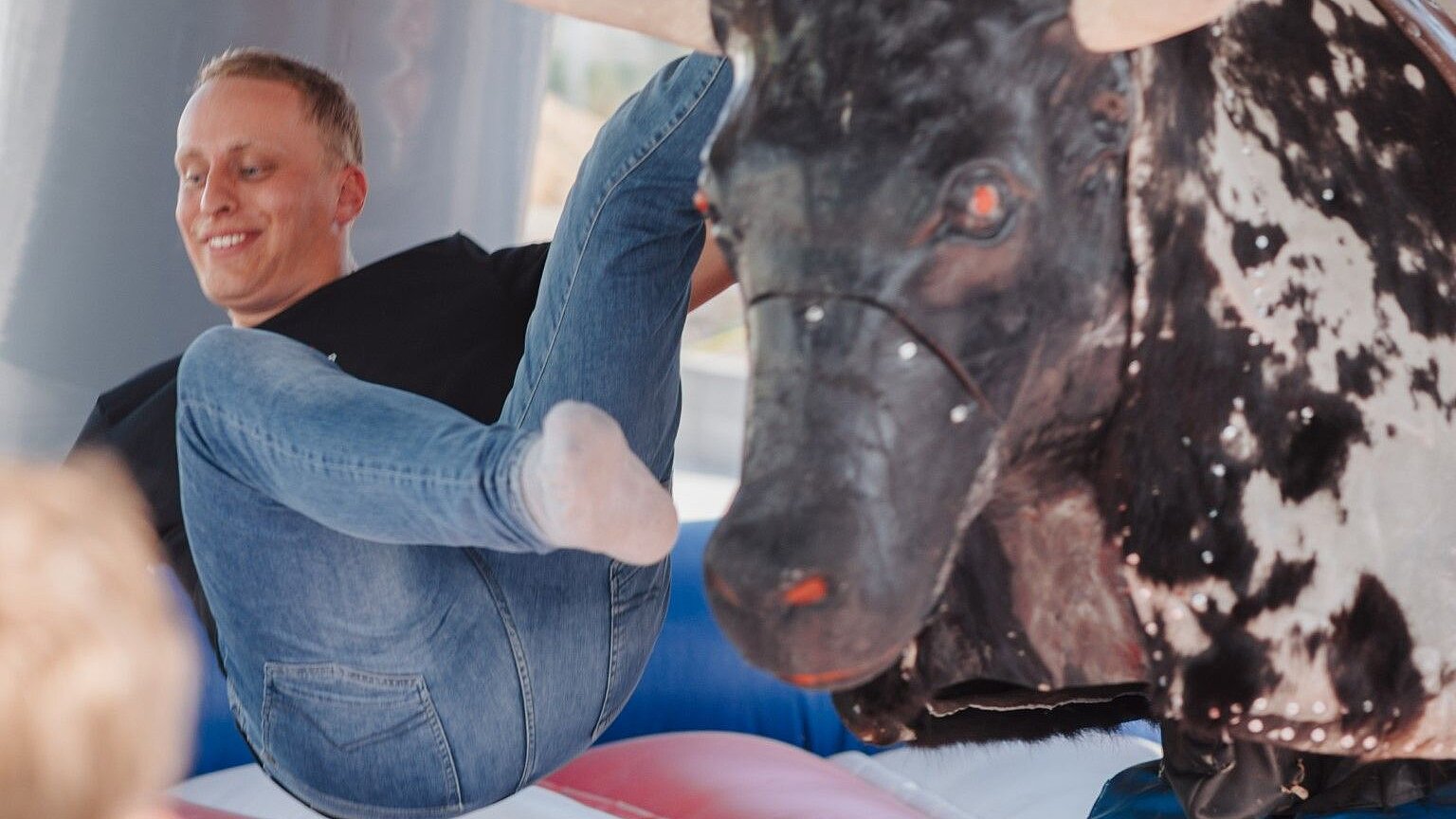 A person falls from a mechanical bull onto a padded surface in an amusement park.