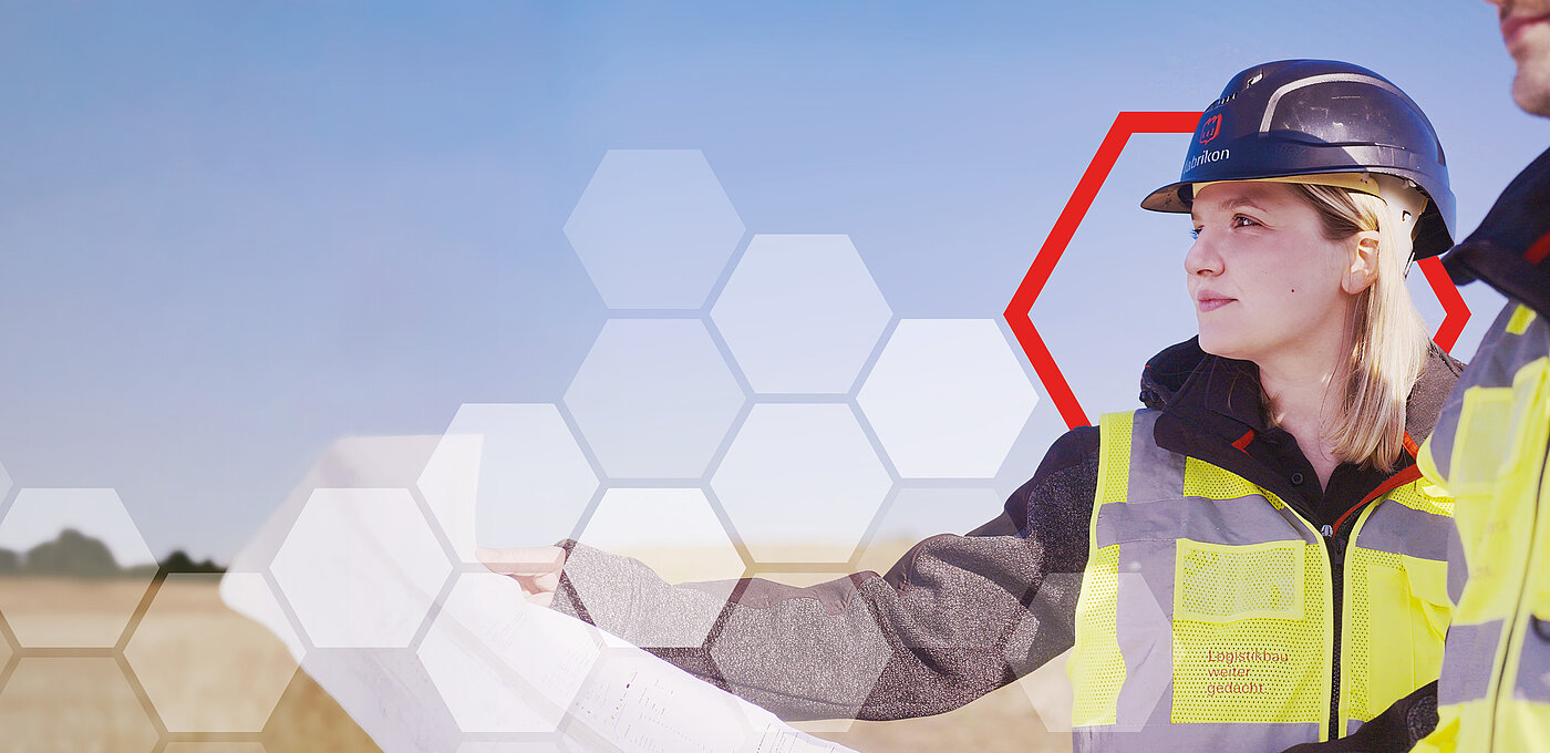 Construction manager wearing a helmet and high-visibility vest looks at plans in a rural setting, with a blue sky in the background.