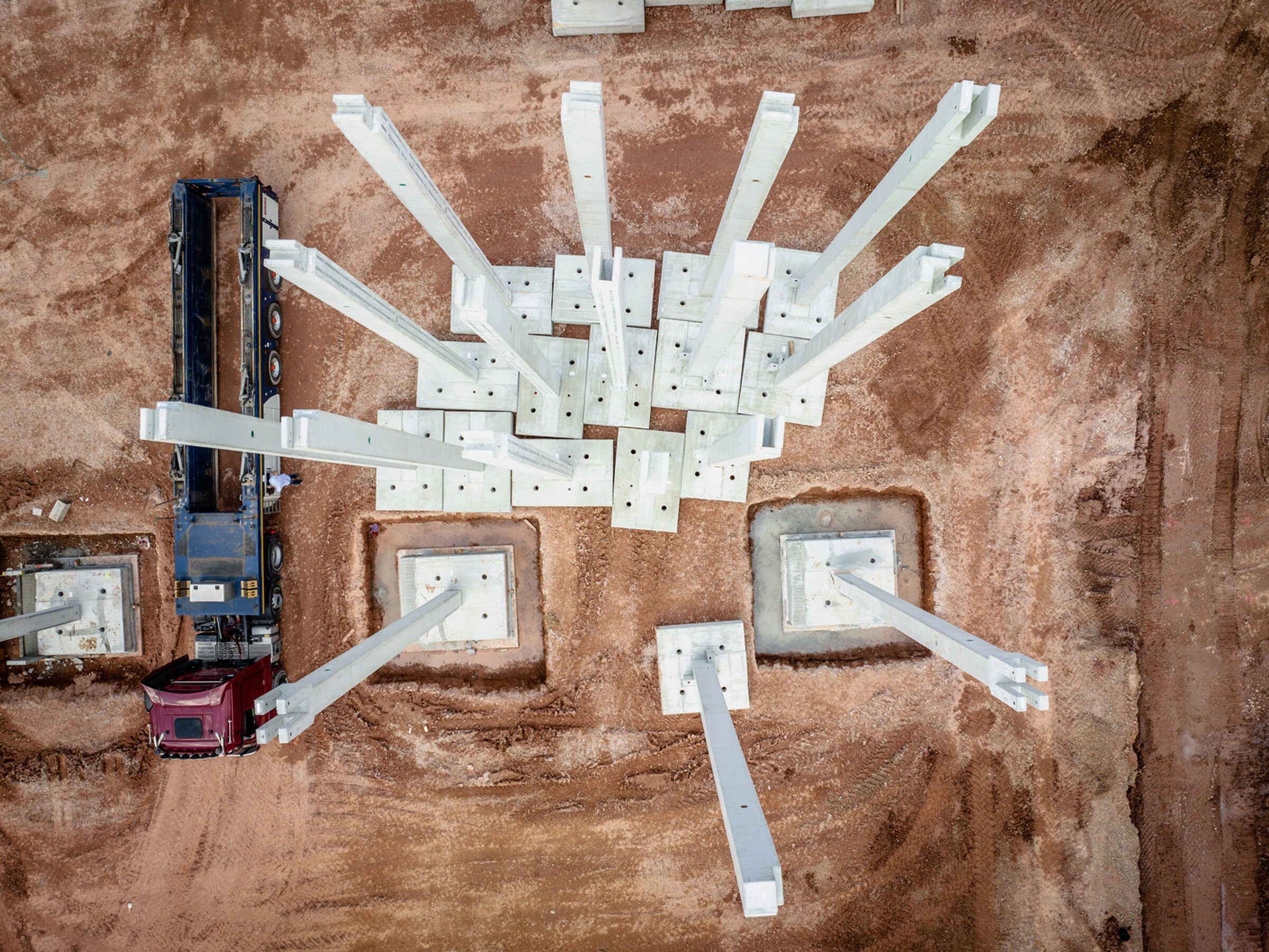 Blick aus der Vogelperspektive auf eine Baustelle mit Betonstützen und einem Lkw neben einer Erdecke.