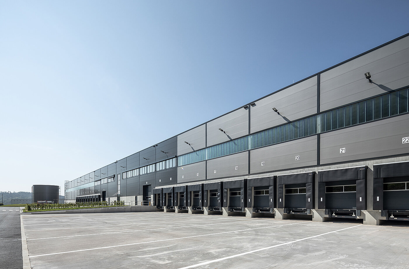 Warehouse building with loading ramps and parking spaces under clear skies. Modern architecture, industrial use.