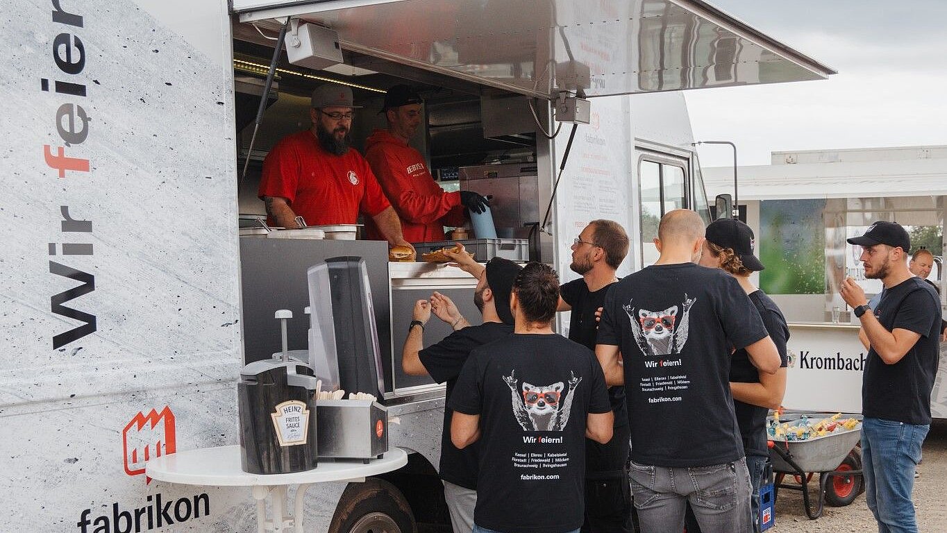 Food truck with employees in red shirts serving food, surrounded by guests in black T-shirts.