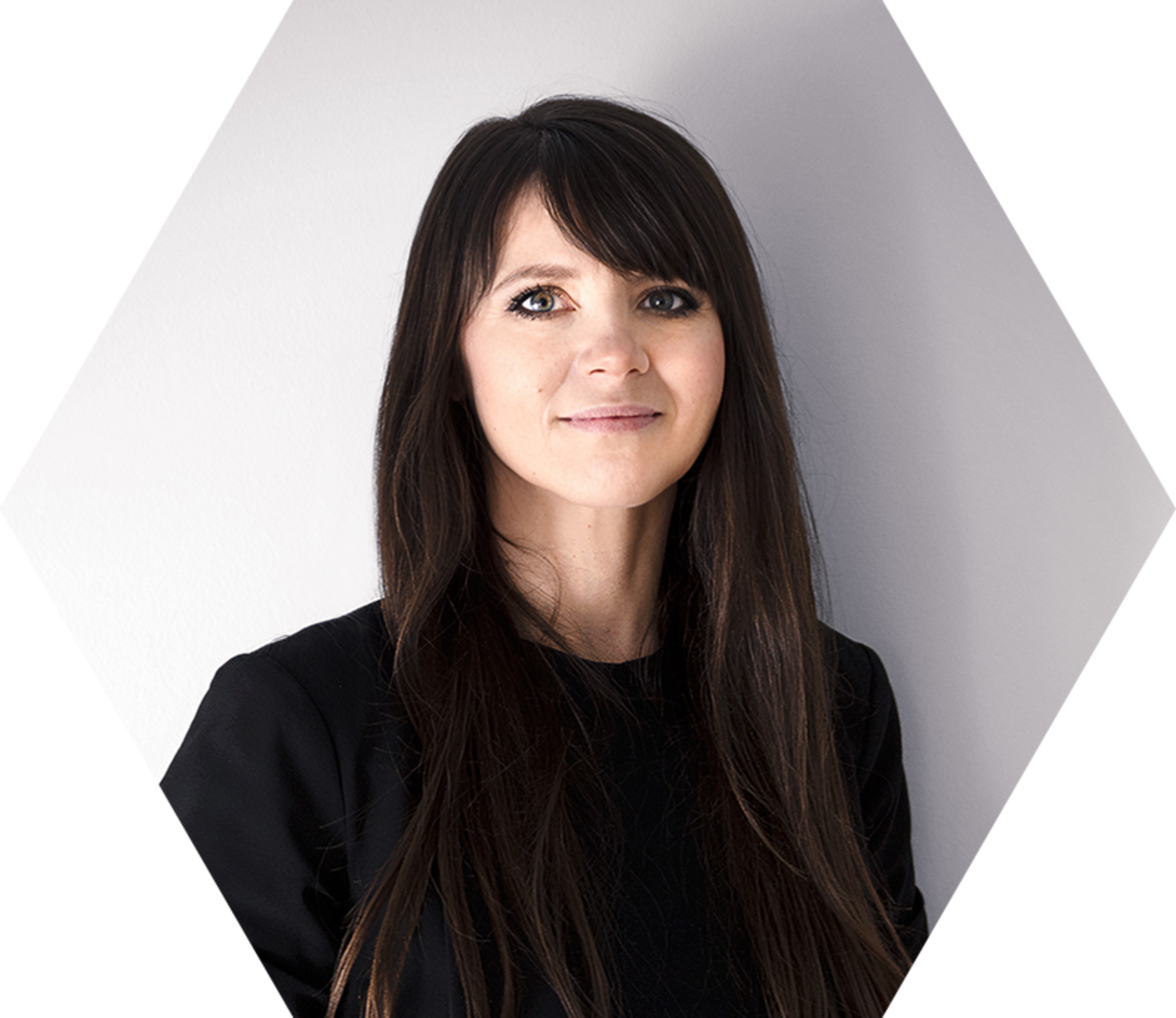 Porträt einer Frau mit langen, dunklen Haaren, die in die Kamera lächelt, vor einem hellen Hintergrund.