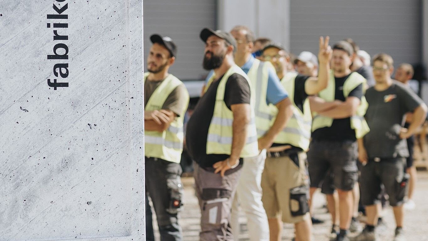 Group of workers in high-visibility vests standing in a row and looking at a parked truck with advertising on it.