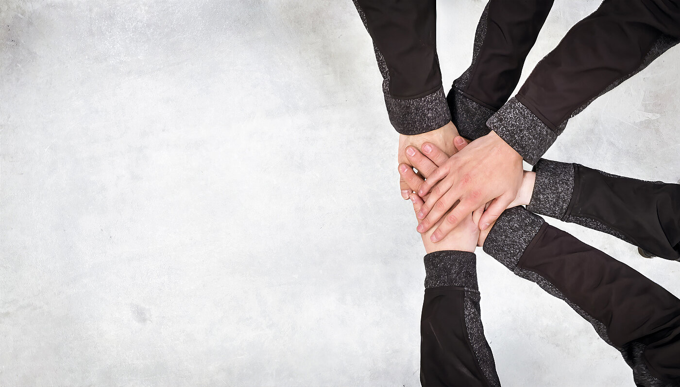 Hands of different people lie on top of each other on a light surface, symbolizing cooperation and team spirit.