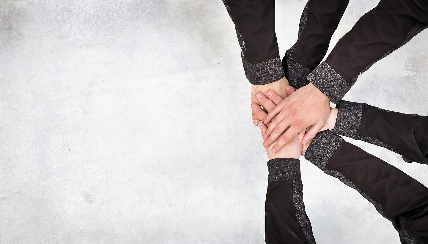 Hands of different people lie on top of each other on a light surface, symbolizing cooperation and team spirit.
