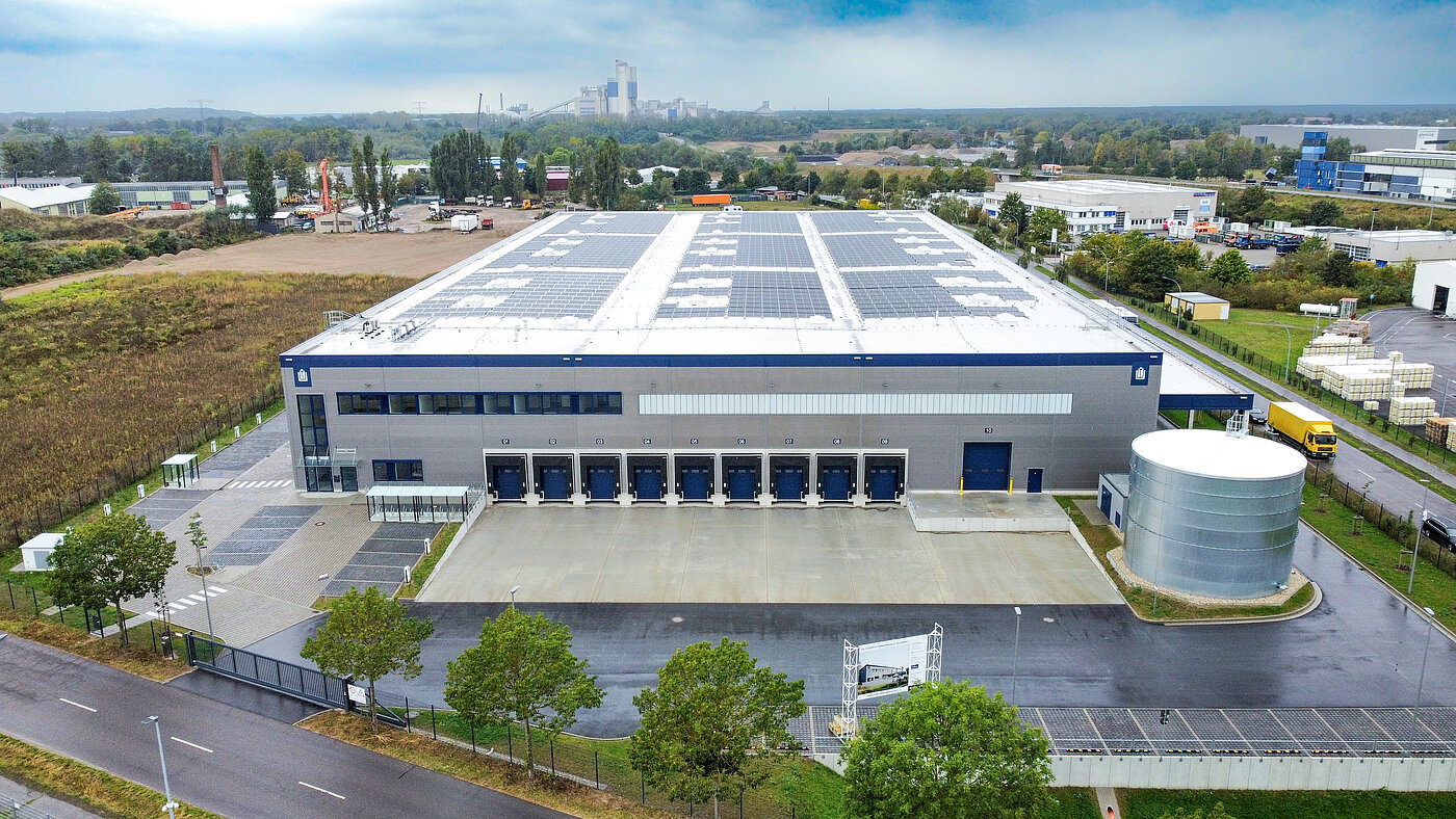 Blick auf ein modernes Lagergebäude mit Solarpanels und Lieferdocks in einer ländlichen Umgebung.