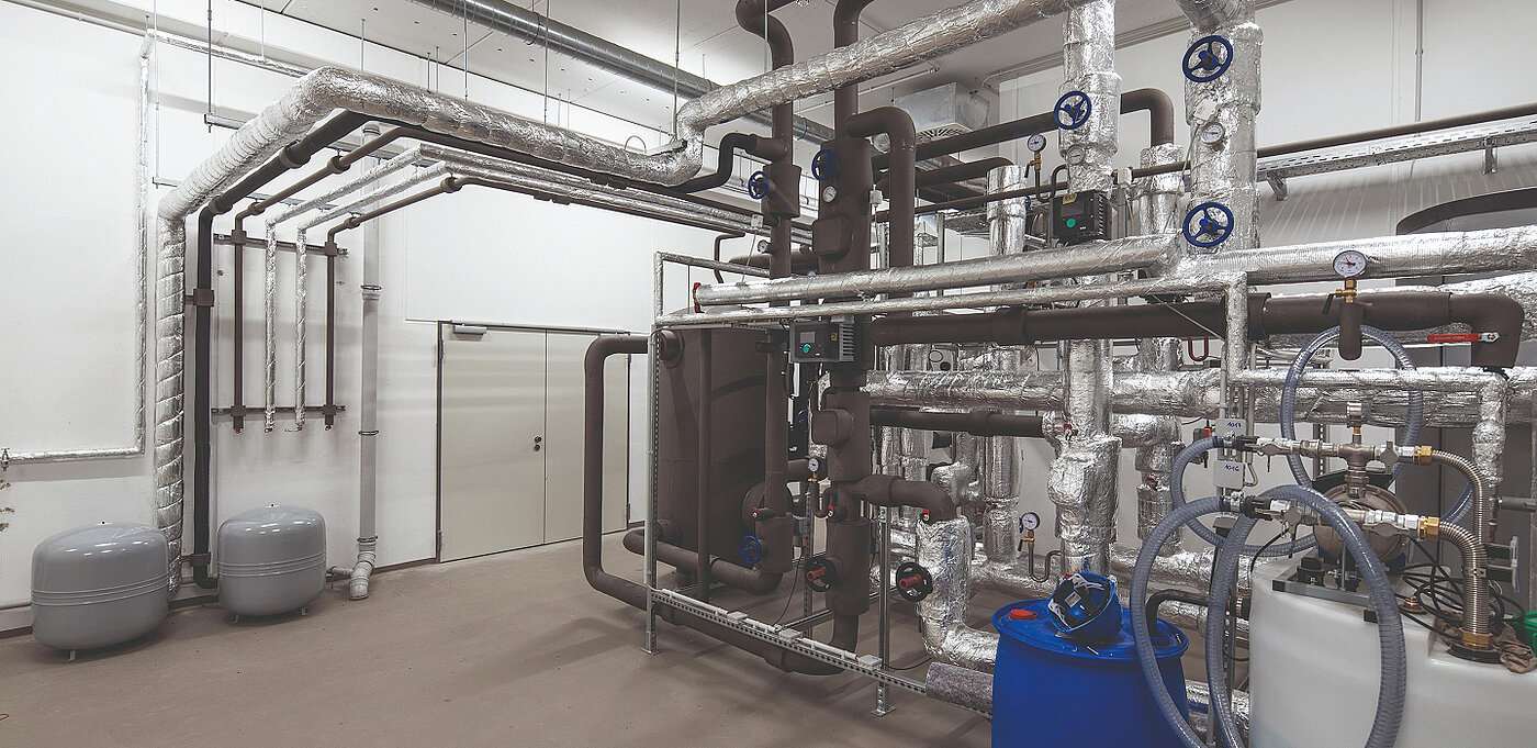 Technische Installation mit Rohren, Ventilen und Tanks in einem Industrieumfeld, alles in einem hellen Raum.