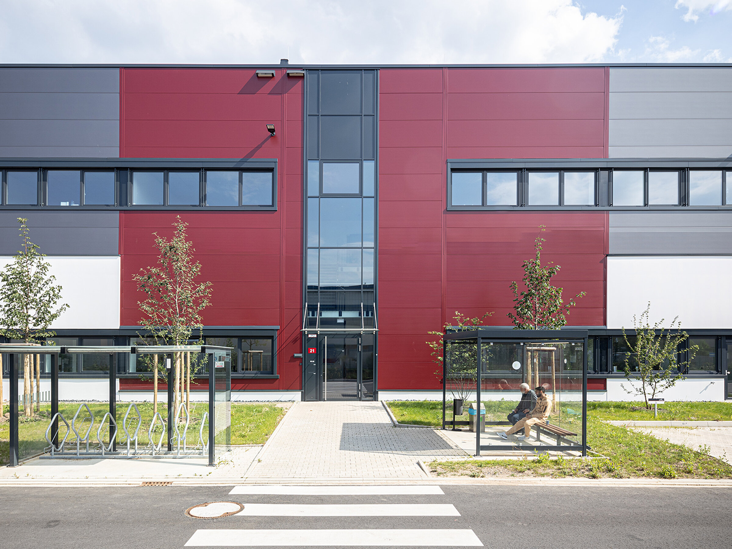 Moderne Gebäude mit farblich gestalteter Fassade, Eingangsbereich und Bushaltestelle im Vordergrund.