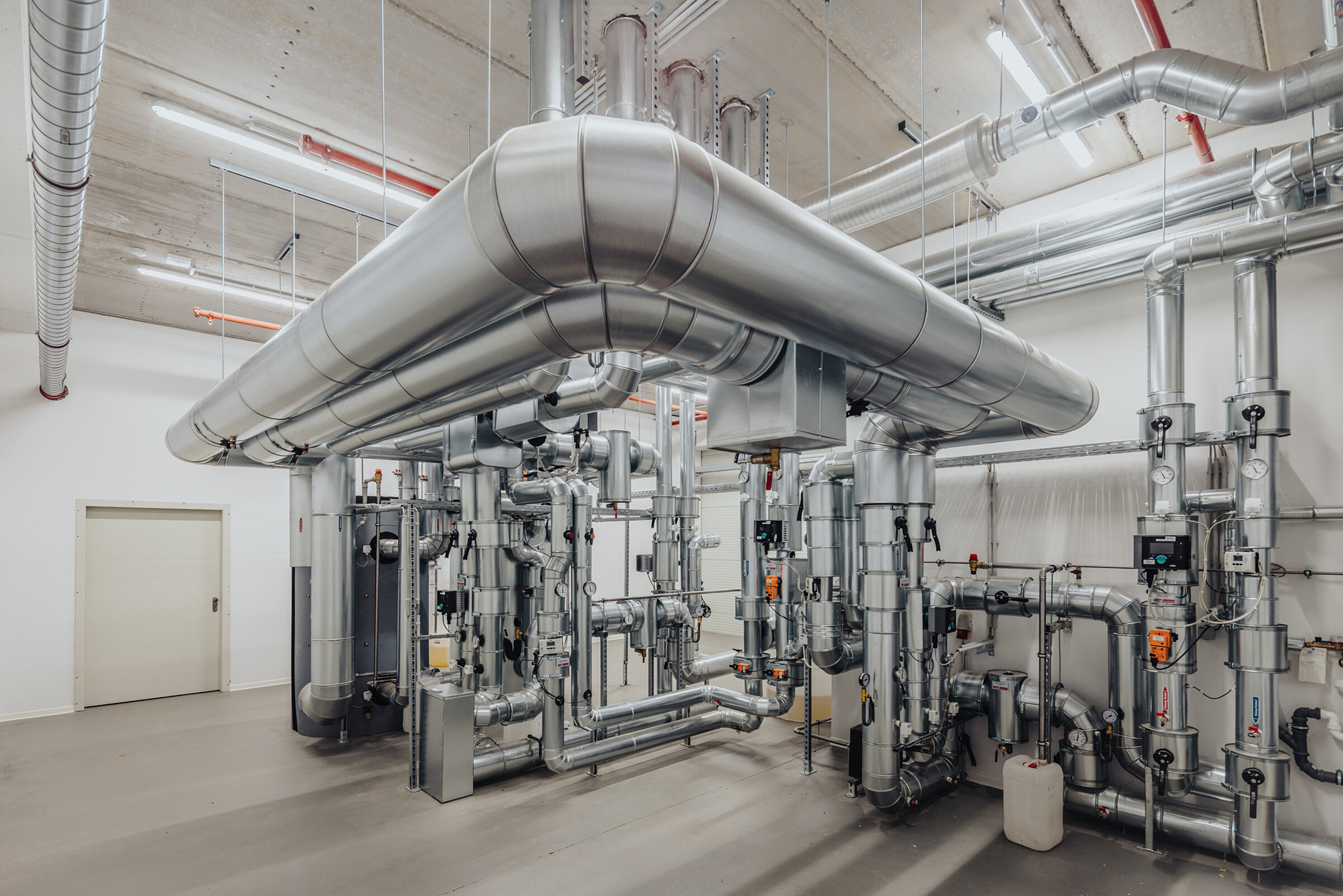Raum mit metallischen Rohrleitungen und technischen Anlagen, die für Gebäudetechnik eingesetzt werden.