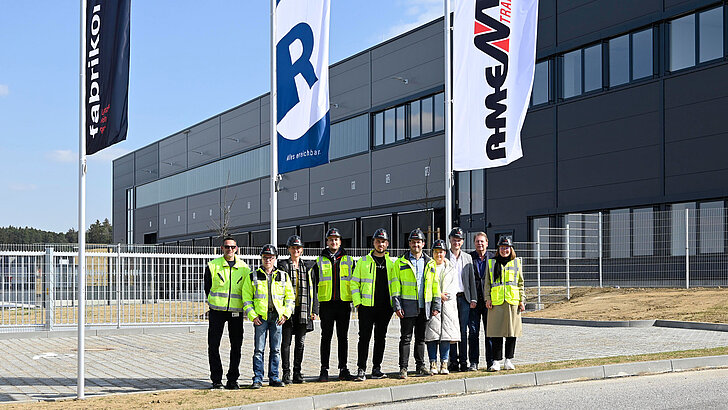 Die Projektbeteiligten am Logistikbau stehen mit Warnwesten zur Schlüsselübergabe vor dem Eingangsbereich an der Nordfassade nach erfolgreicher Übergabe