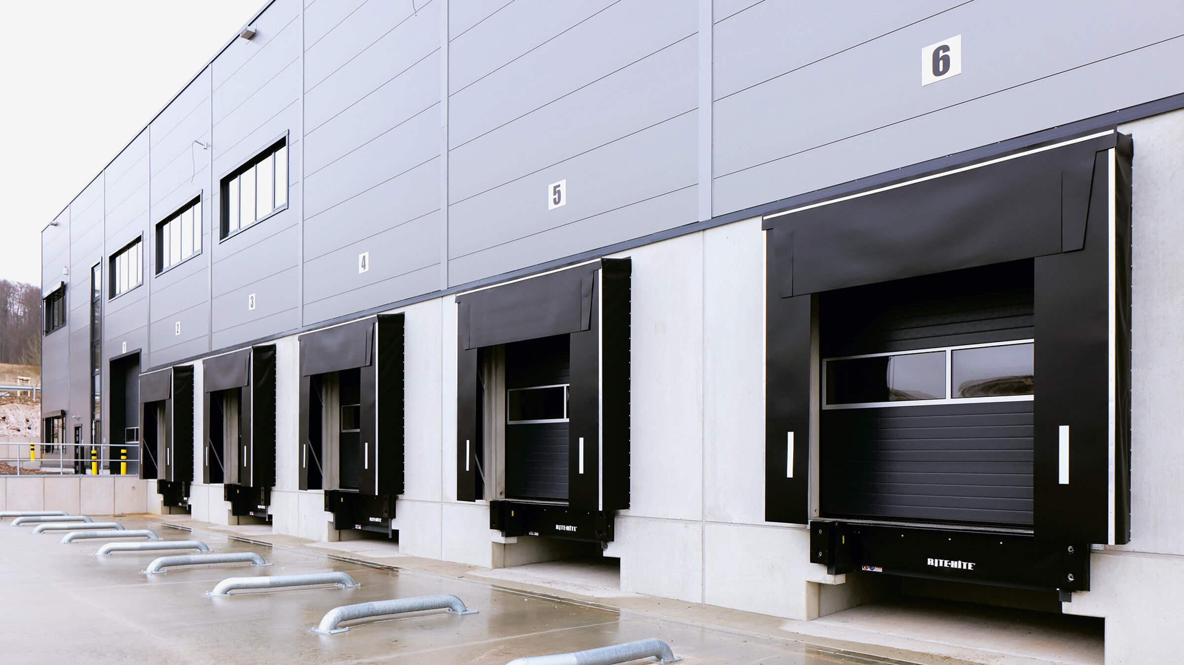 Moderne Lagerhalle mit mehreren Laderampen und nummerierten Fenstern an der Fassade. Graue Wände, Rampen sind ungenutzt.