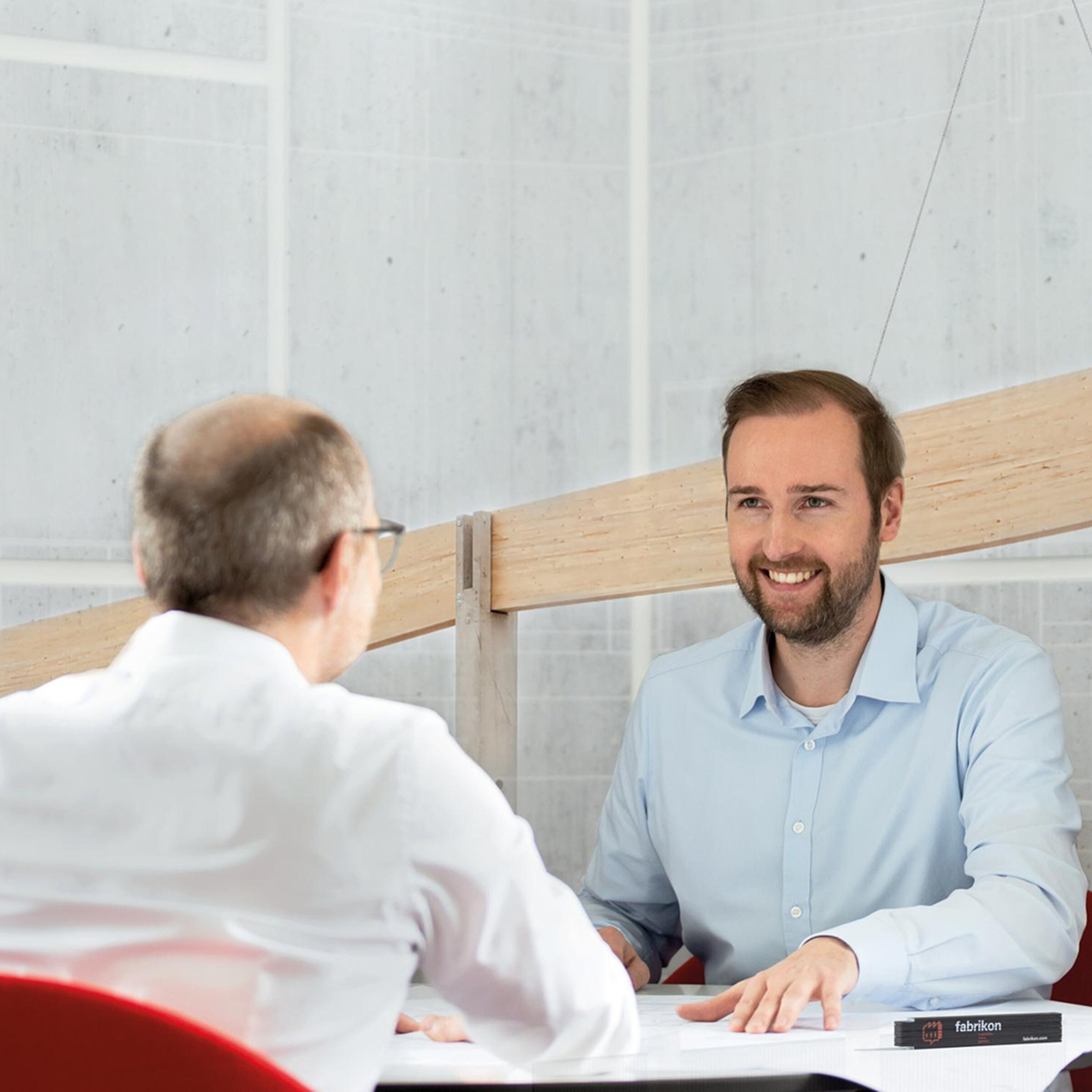 Zwei Personen sitzen an einem Tisch in einem modernen Büro und führen ein Gespräch. Beide lächeln freundlich.