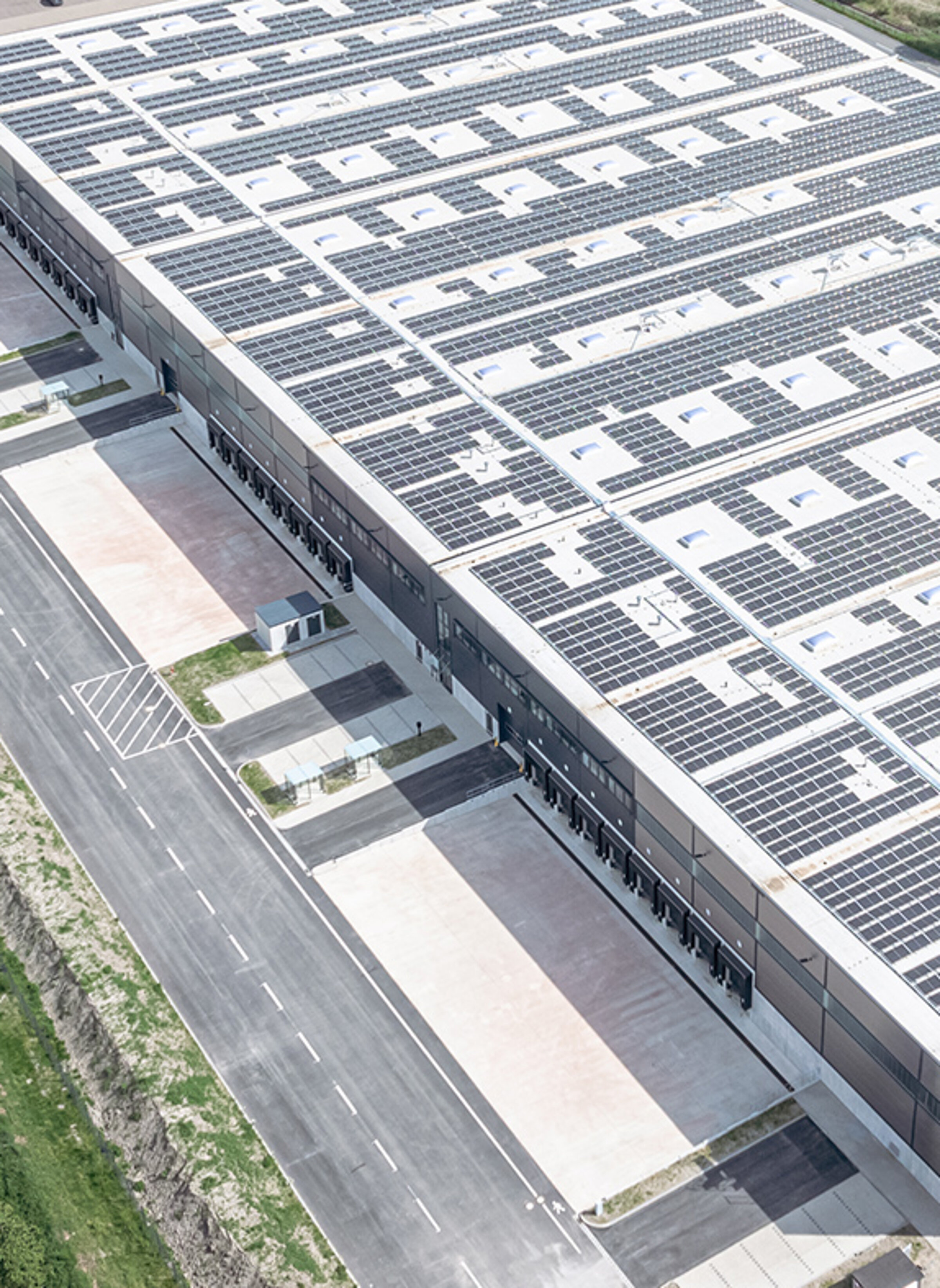 Luftaufnahme eines modernen Gebäudes mit Solarpanels, umgeben von Straßen und Grünflächen.