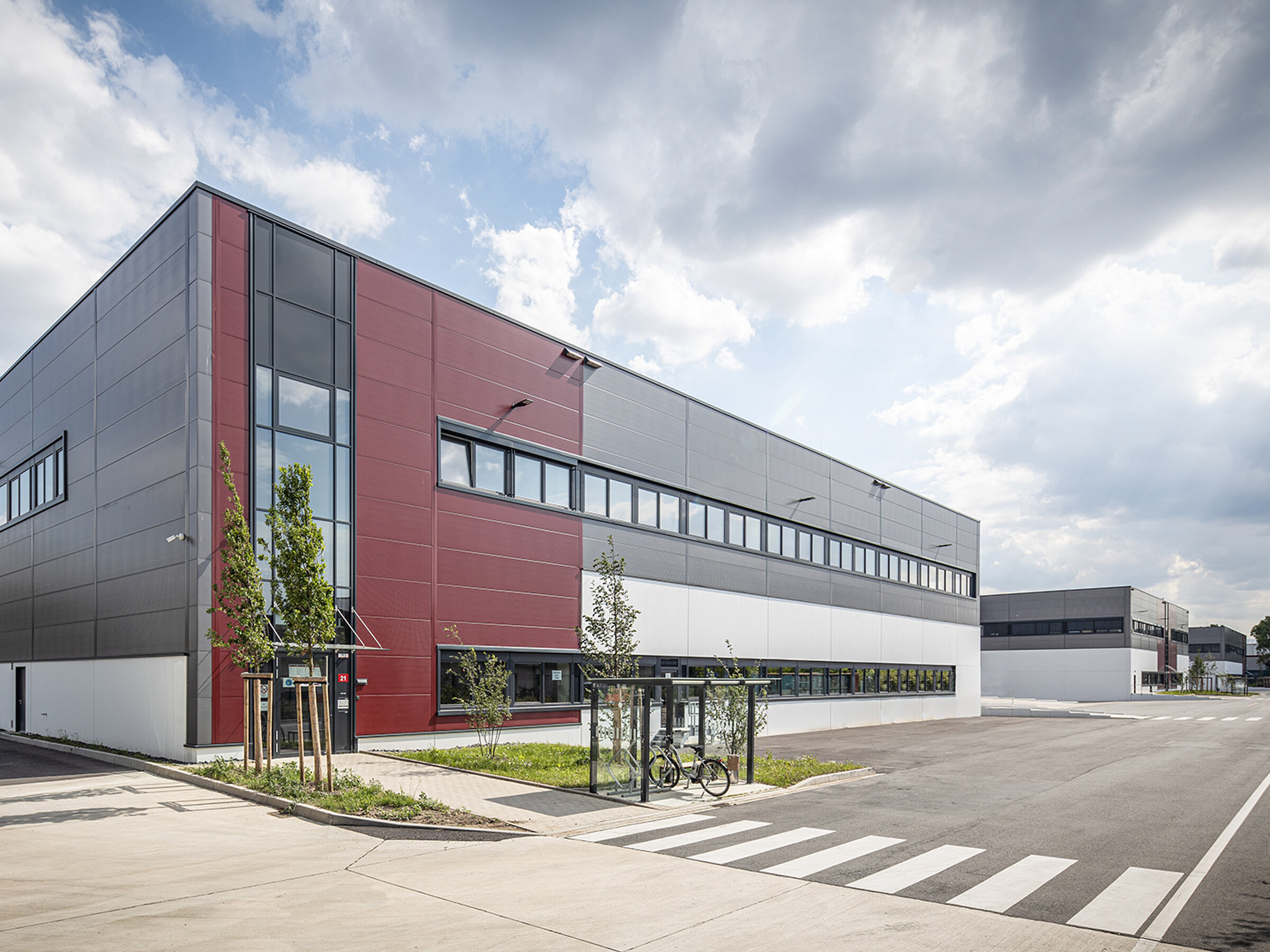Moderne Lagerhalle mit großzügigen Fenstern und einem klaren Design, umgeben von einer Zufahrt und Stadtlandschaft.