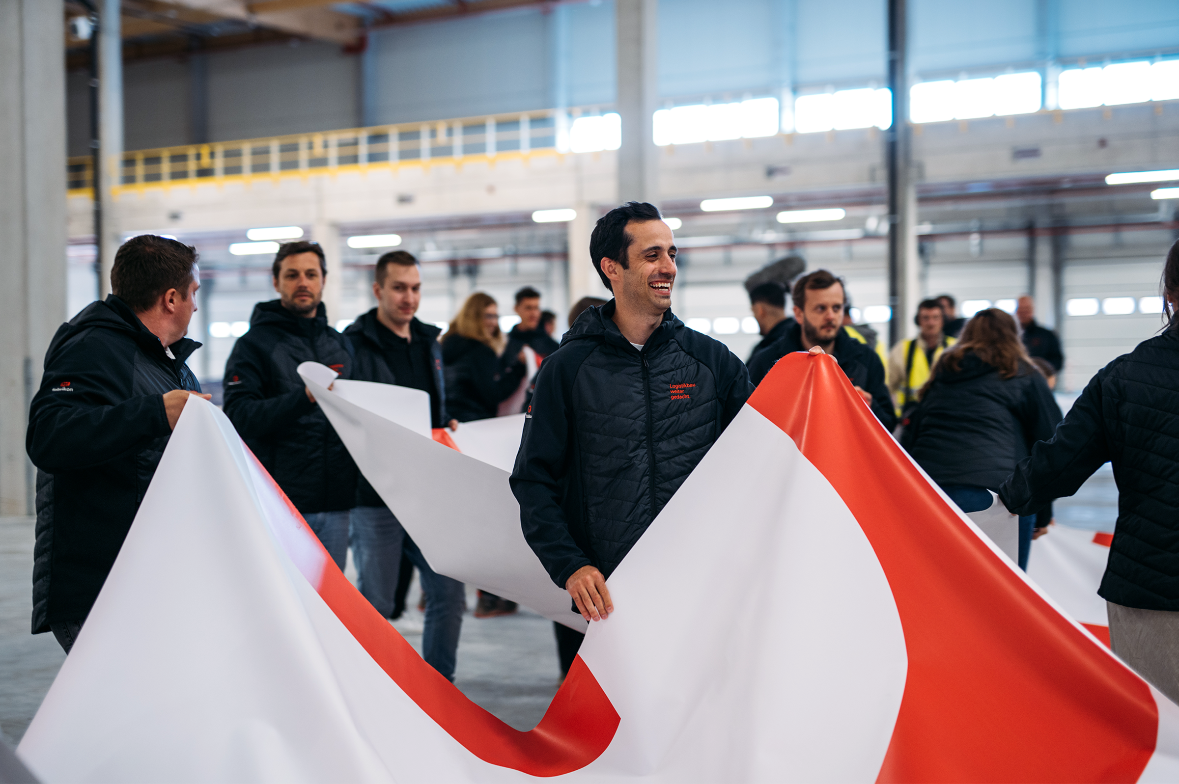 fabrikon Mitarbeitende führen bei einer Teamveranstaltung in einer modernen Logistikhalle eine gemeinsame Gruppenaktivität durch.