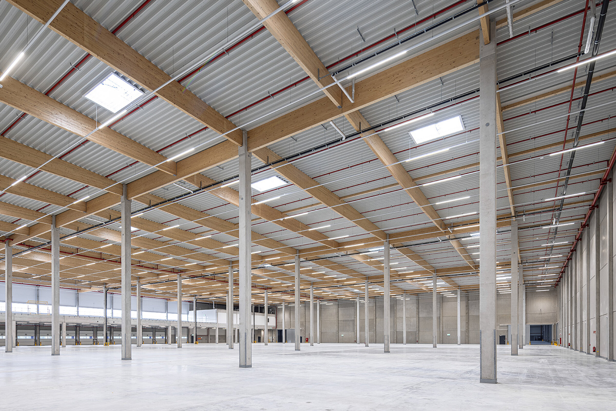 Luftiger Lagerraum mit hohen Decken, Holz- und Stahlträgern sowie großen Fenstern, die Tageslicht einlassen.