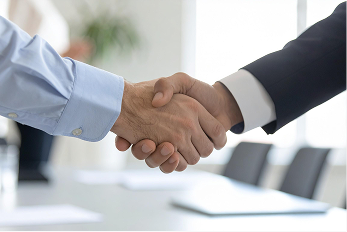 Zwei Personen schütteln sich die Hände in einer Büroumgebung, Symbol für eine Vereinbarung oder Zusammenarbeit.