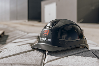 Schwarzer Schutzhelm mit Logo „fabrikon“, auf einem grauen Stein im Außenbereich platziert.