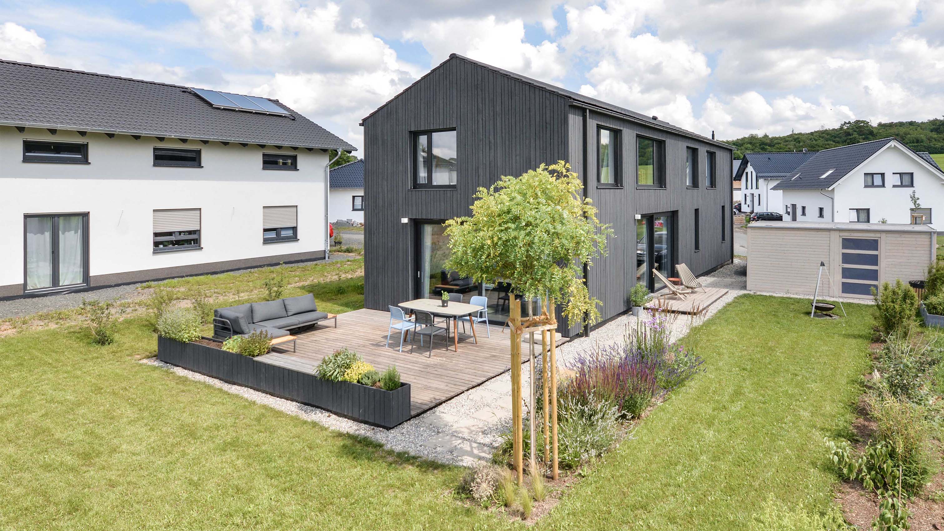 In dunkler Holzverschalung verkleidetes, minimalistisches Satteldach-Haus mit Terrasse und Garten