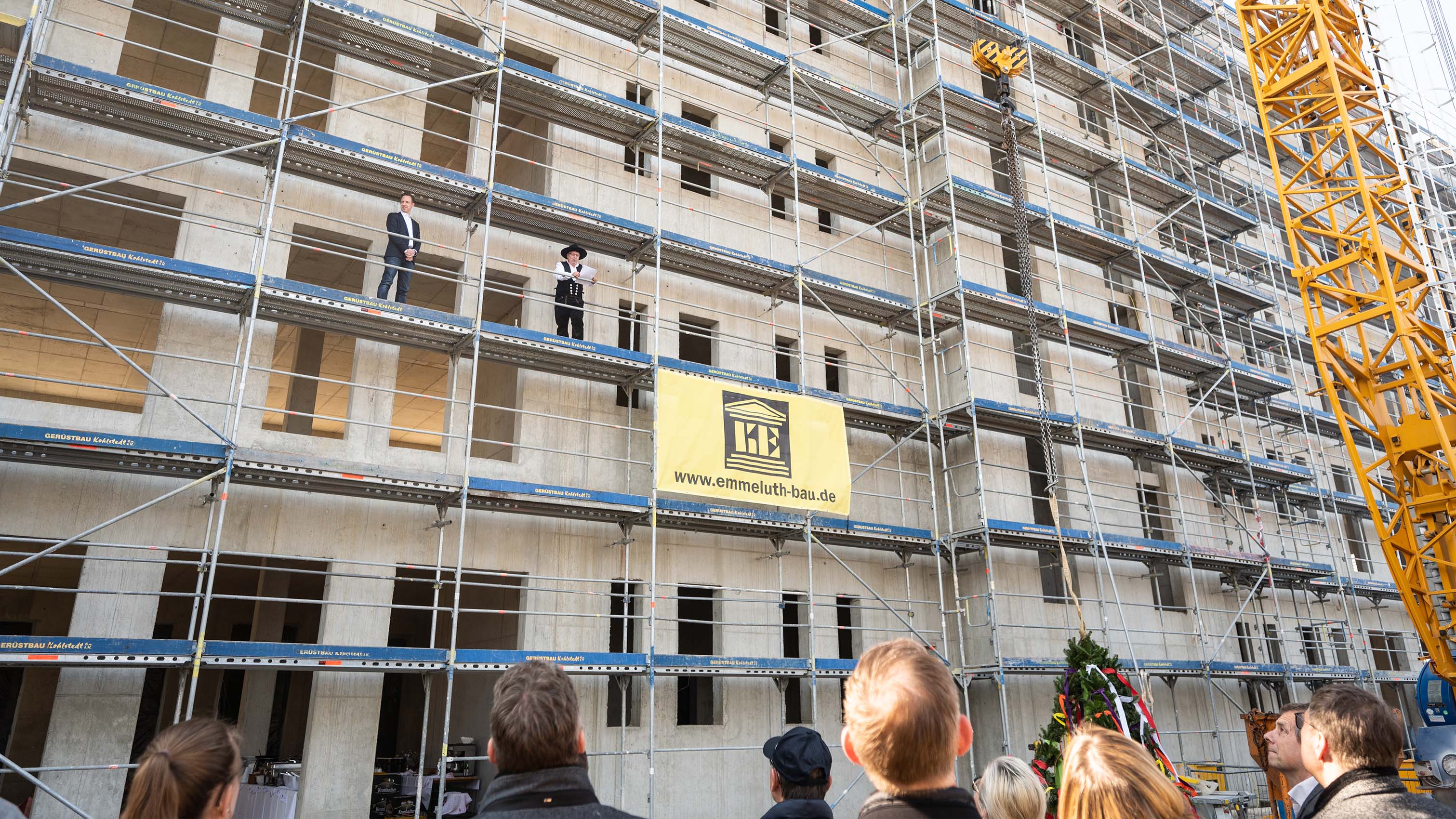 Ein Zimmermann hält den Richtspruch hoch oben auf dem Gerüst 