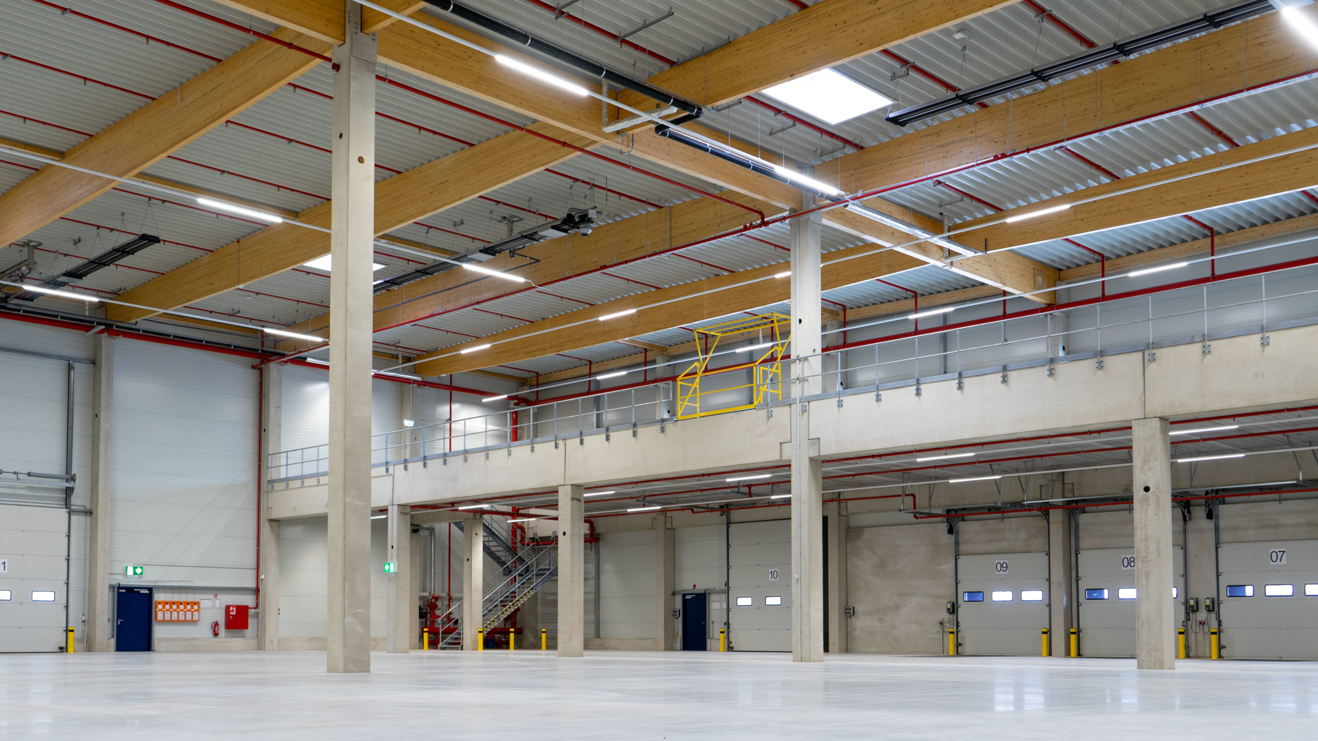 alt=" fabrikon logistics hall in Berlin Herzfelde, interior view of the hall with a view of the timber roof structure, the mezzanine and the overloading doors."