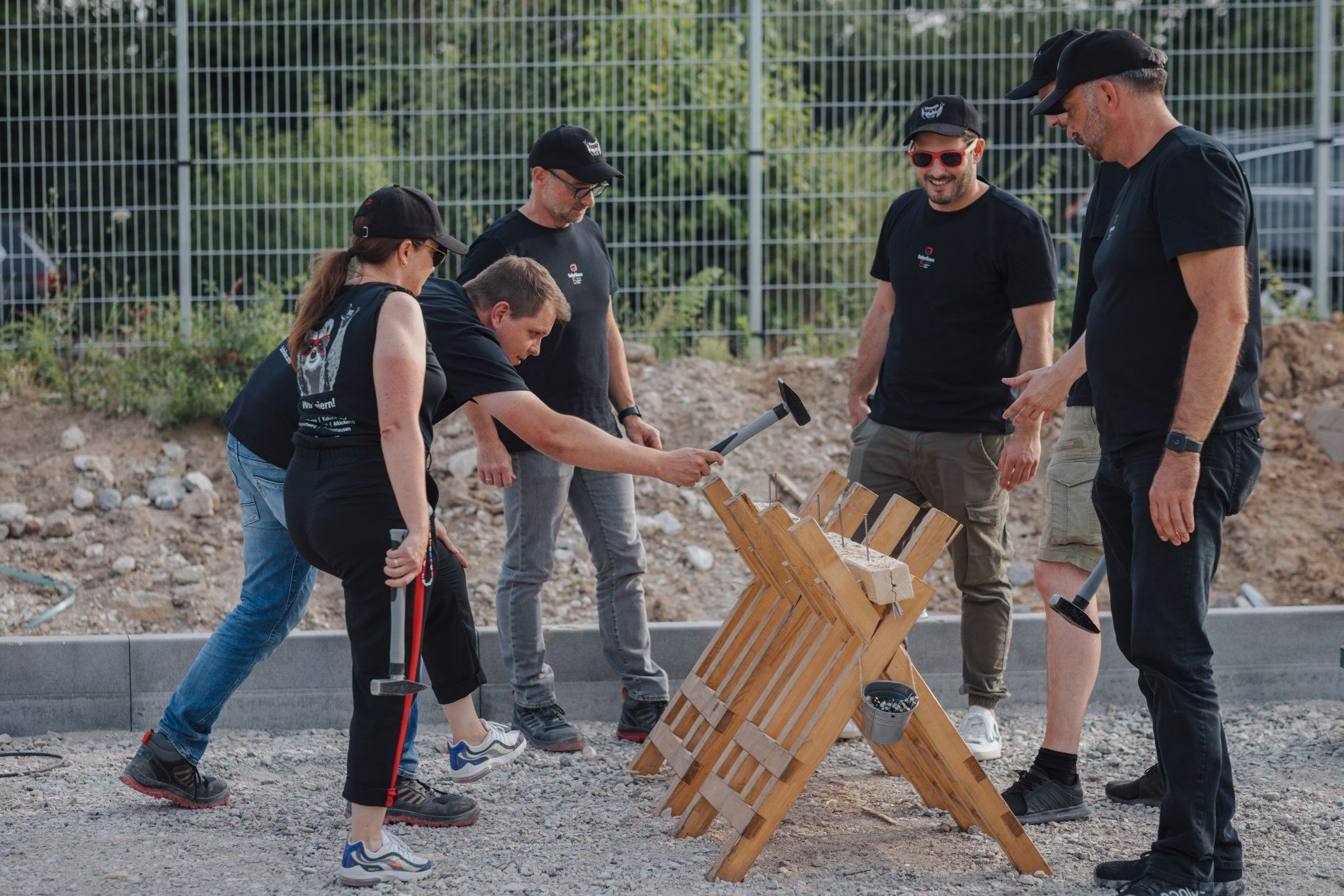 Six people are working together on a wooden scaffold, while one of them is hitting the wood with a hammer.