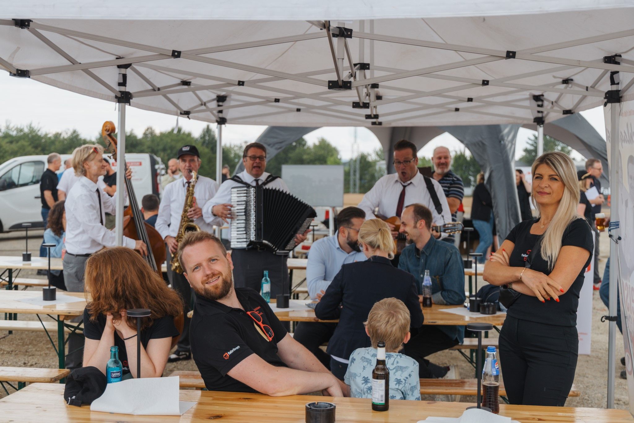 People in a marquee with live music, tables, and drinks, laughing and talking with each other.