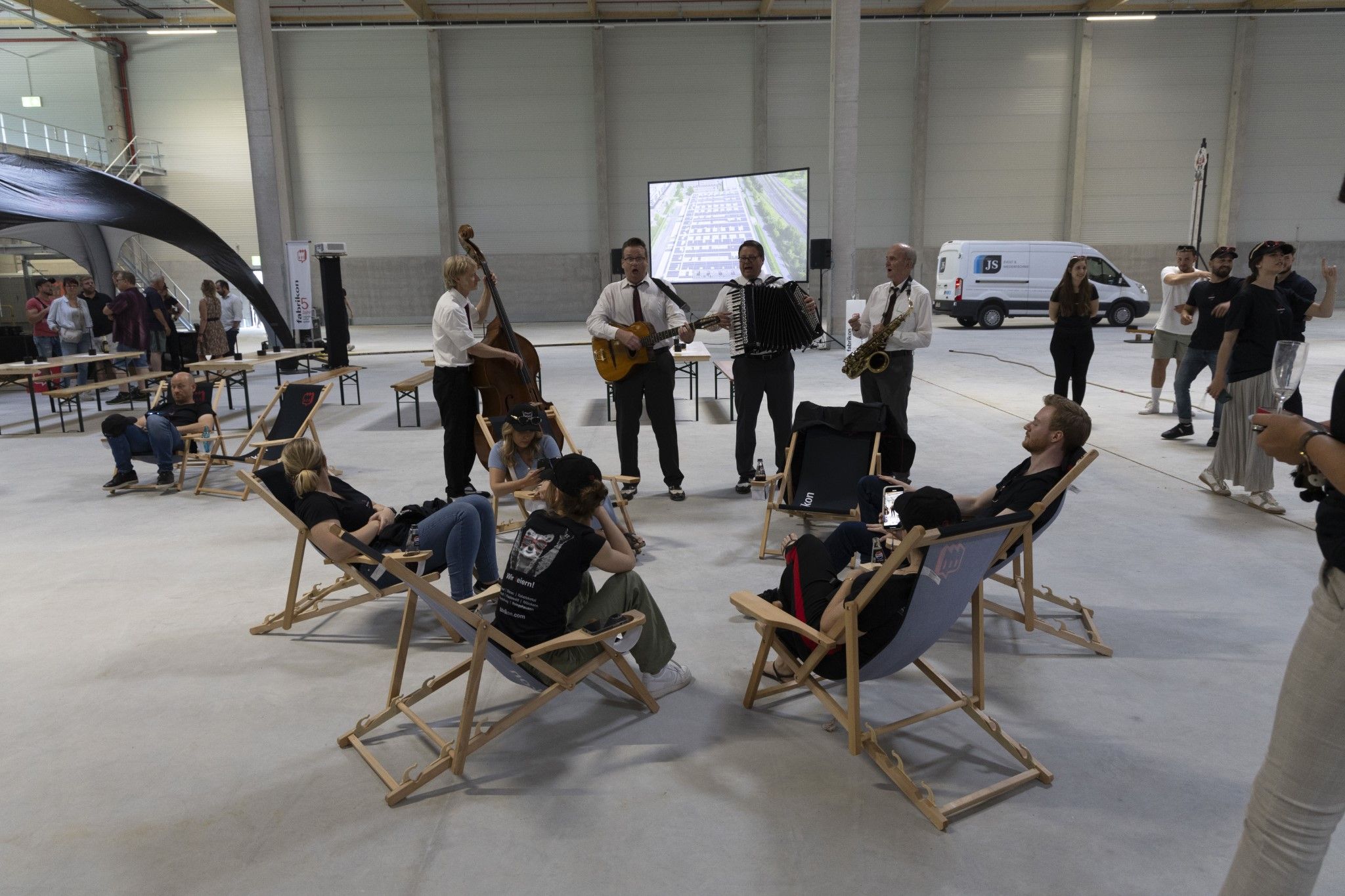 Musicians play in a large room while guests relax in deck chairs and watch.