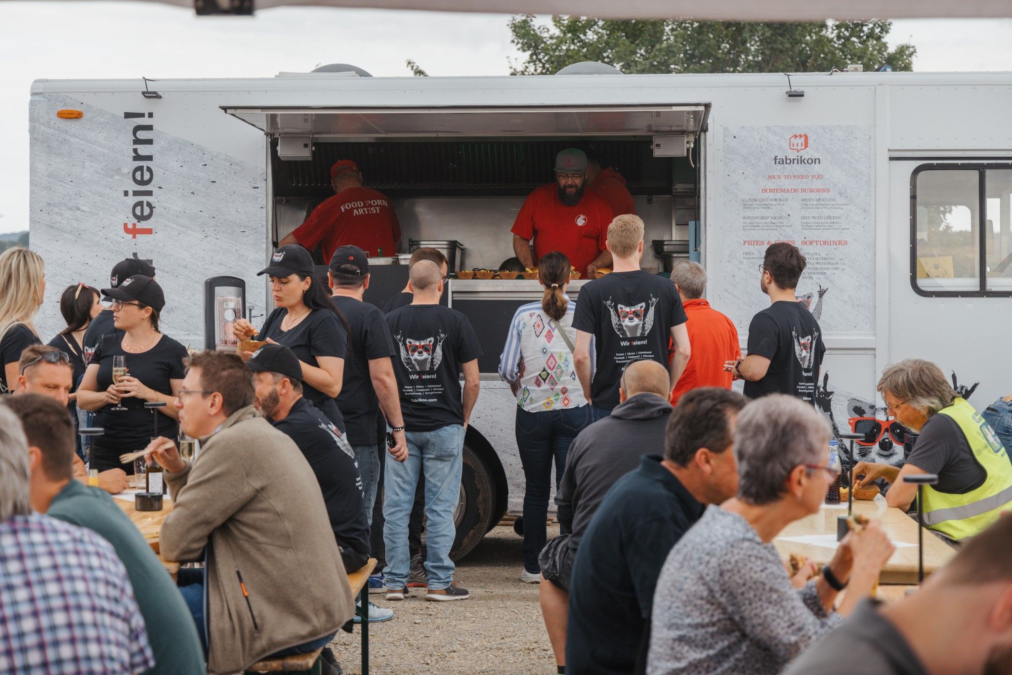 Food truck with people ordering and eating burgers, relaxed atmosphere at an outdoor event.