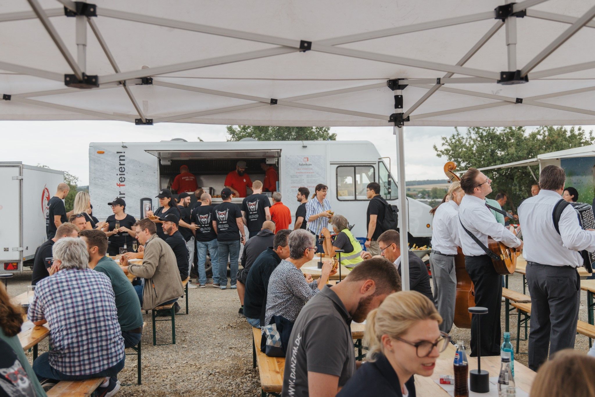 A bustling food truck market with people enjoying food and musicians creating a lively atmosphere.