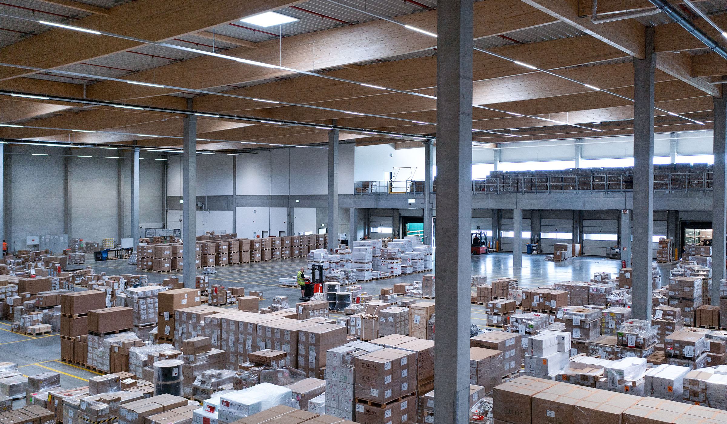 Ein großer Lagerraum mit angeordneten Kisten und Paletten, Mitarbeiter bedienen Geräte zwischen den Regalen.