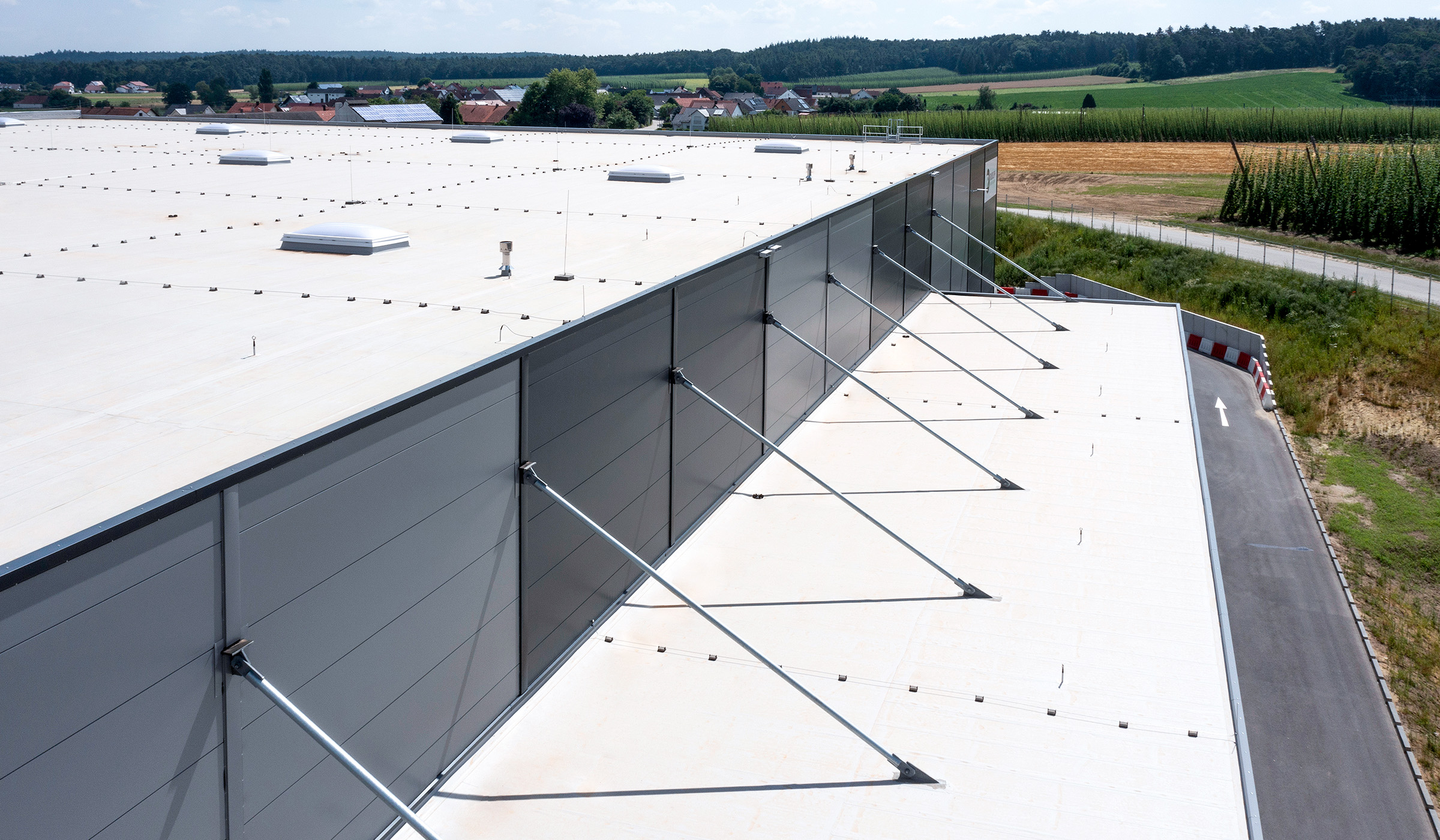 Dachansicht eines großen Gebäudes mit grauer Fassade und Stützstreben, umgeben von einer ländlichen Umgebung.