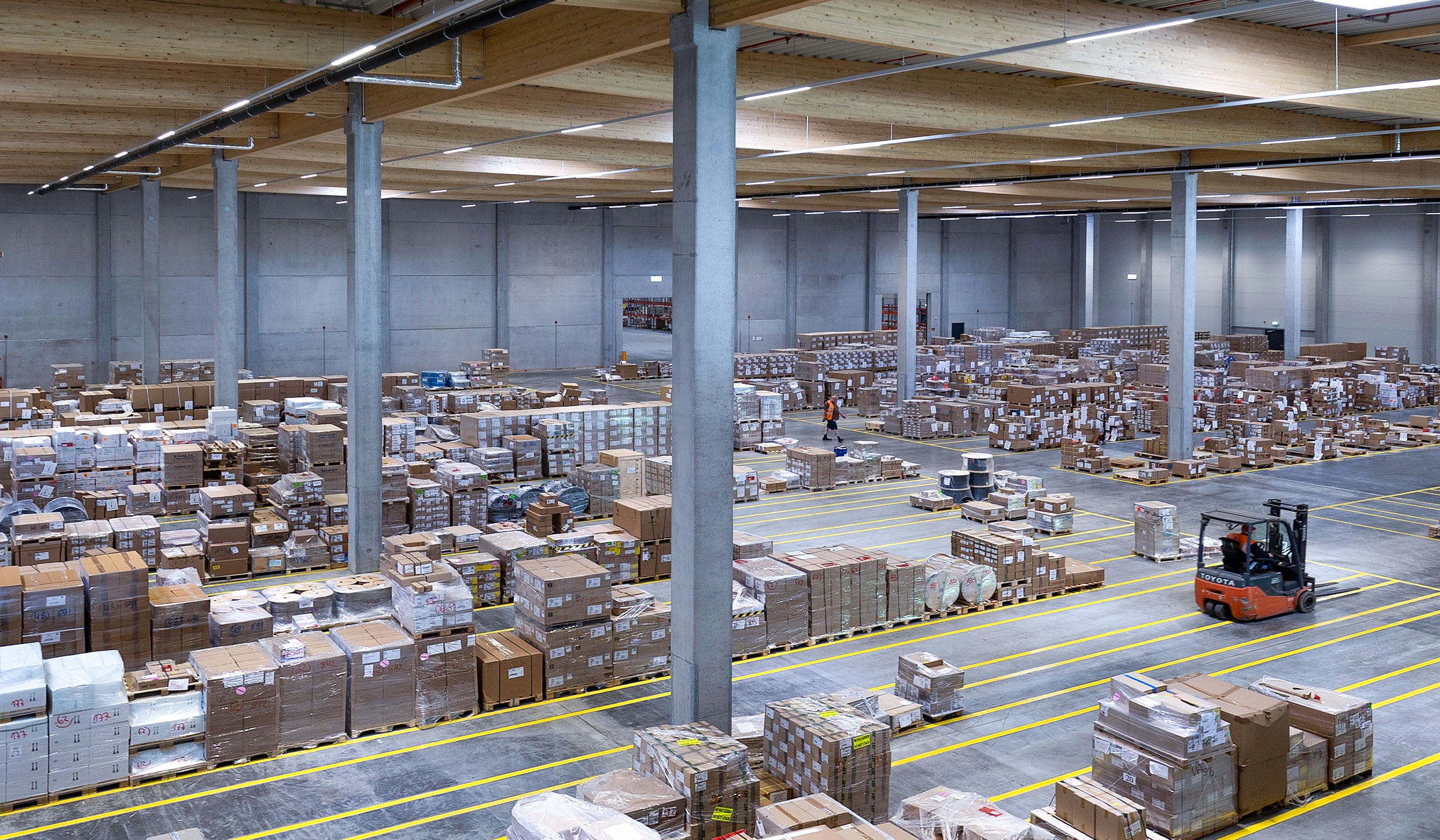 Große Lagerhalle mit vielen Kartons und einem Gabelstapler, der in den Gängen fährt.