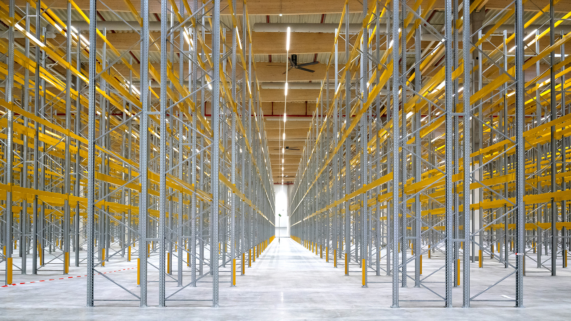 Leere Lagerhalle mit Regalen aus Metall und gelben Tragbalken, beleuchtet von hellen LED-Lichtern.