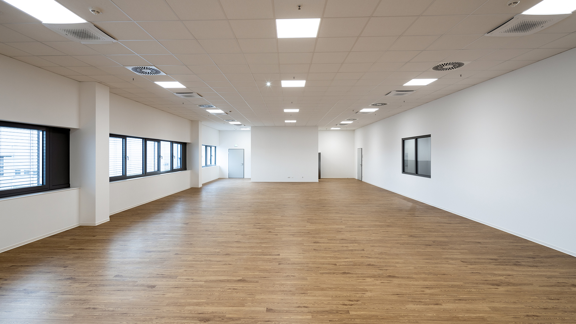 Großer, heller Büroraum mit Holzboden, großen Fenstern und minimalistischem Design.