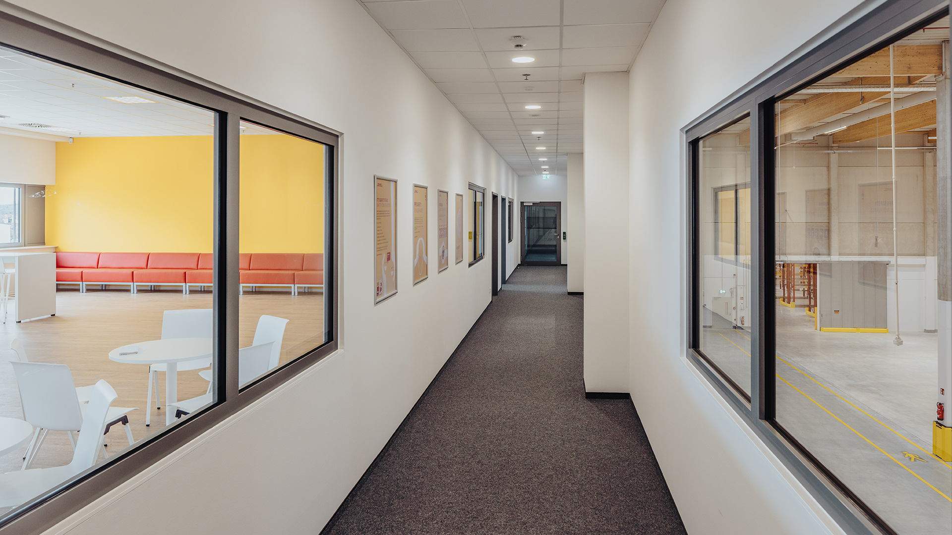 Langer, heller Flur mit Fenstern, geräumigem Wartebereich und bunten Wänden auf der linken Seite.