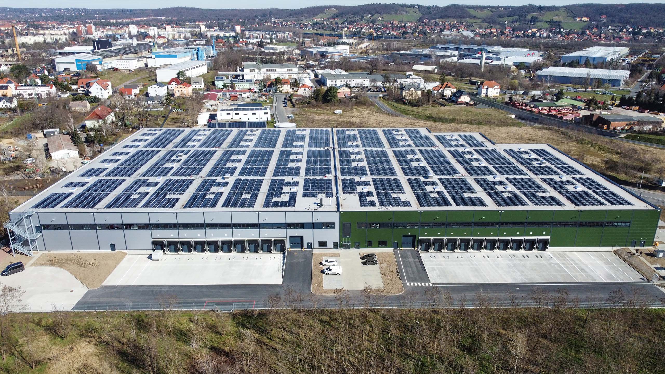 Modernes Lagergebäude mit Solaranlagen auf dem Dach, umgeben von einer städtischen Landschaft.