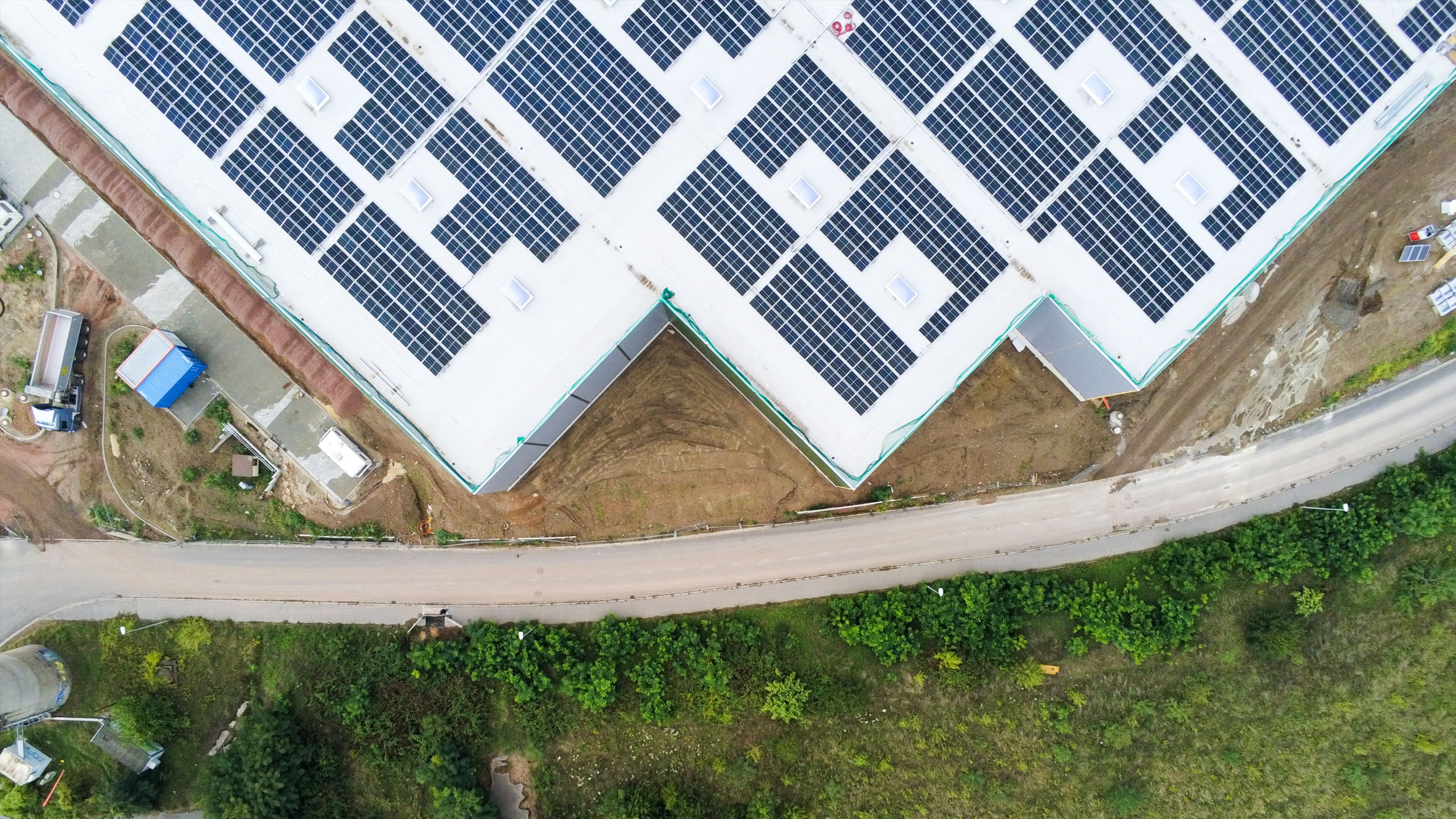 Dachansicht eines Gebäudes mit Solarpanelen, umgeben von Grünflächen und einem Weg.