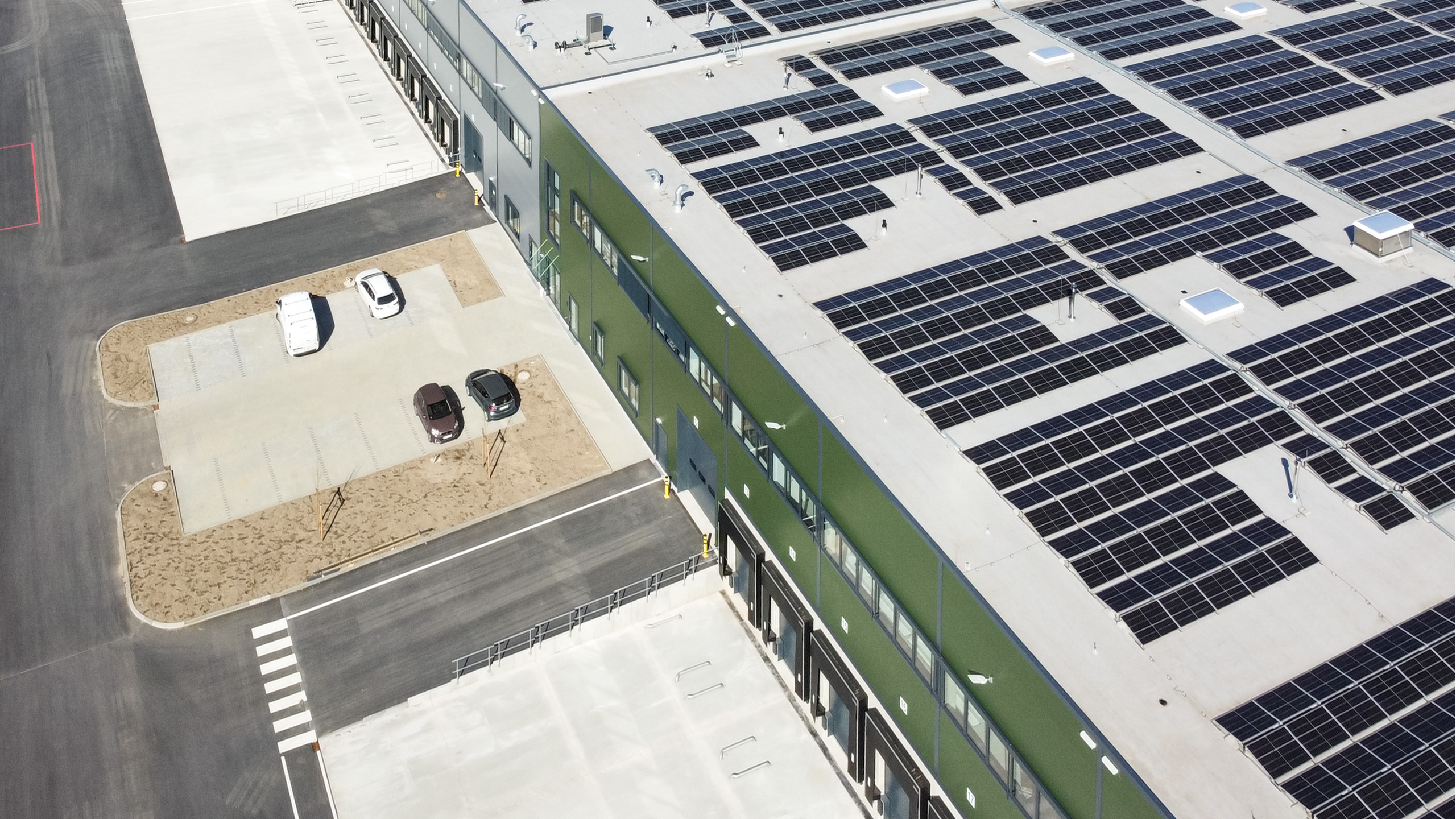 Moderne Lagerhalle mit Solarpanelen auf dem Dach und Parkplatz für PKWs im Vordergrund.