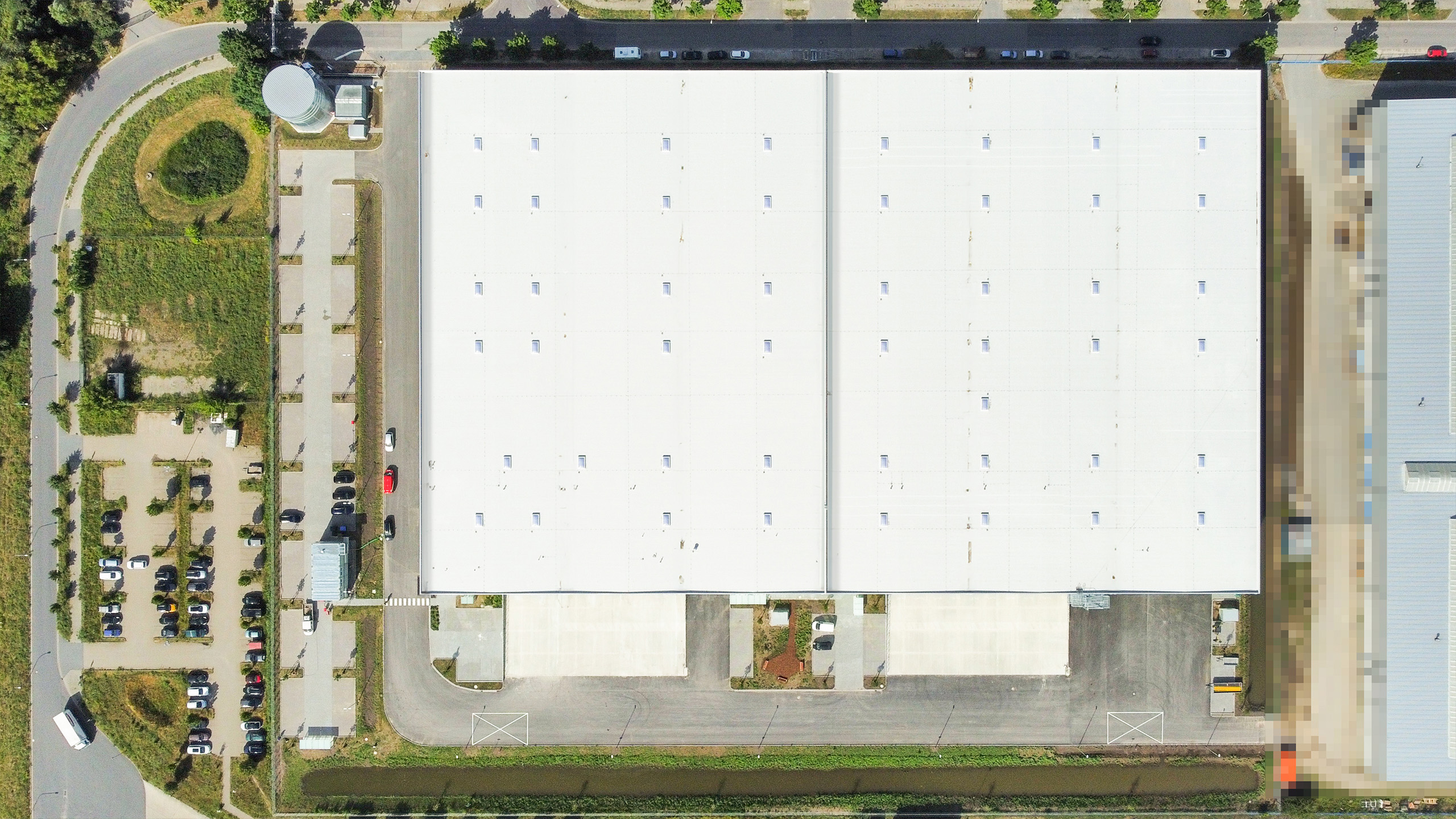 Luftaufnahme eines großen, flachen Gebäudes mit Parkplätzen und umliegenden Grünflächen.