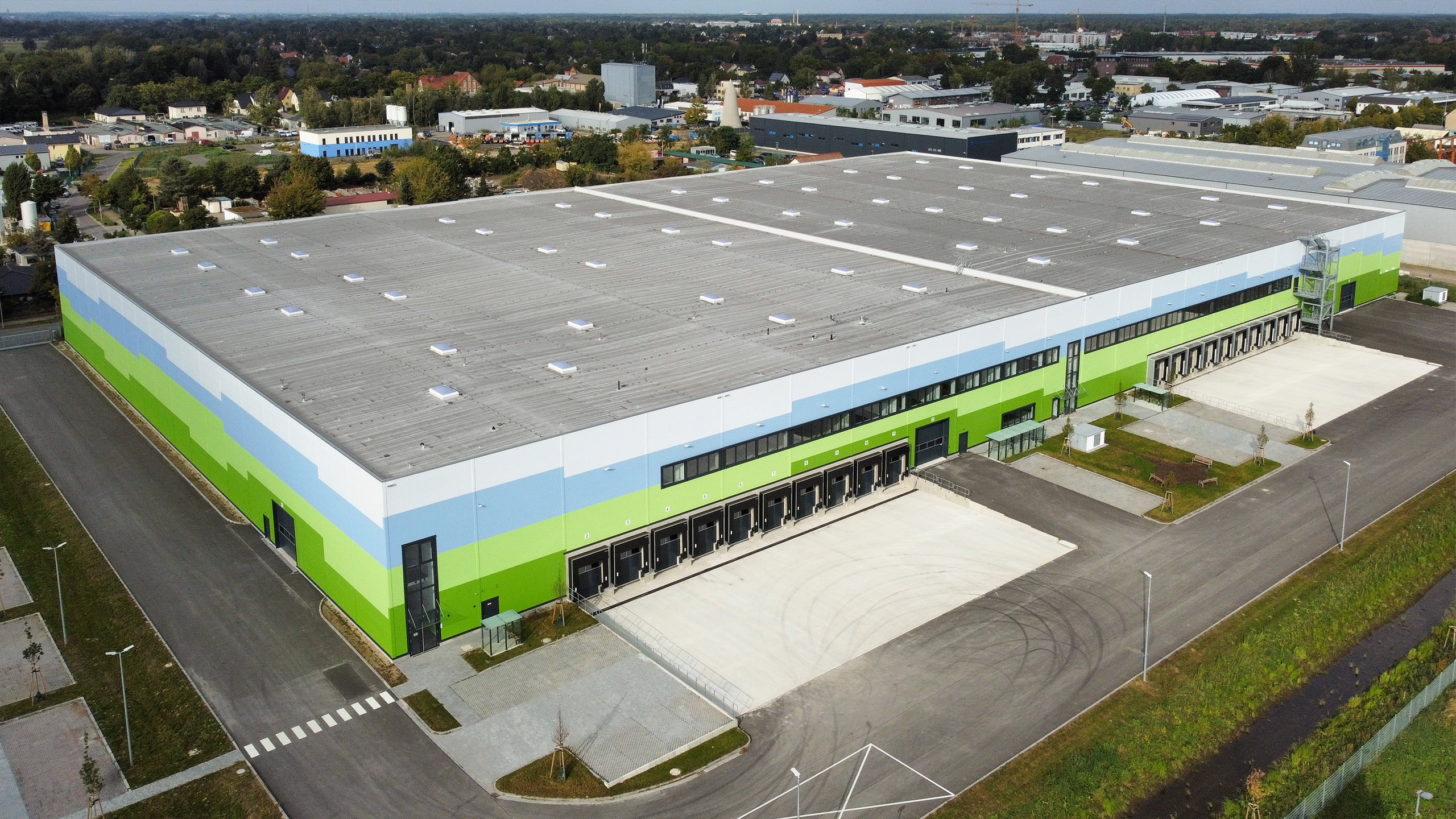Luftaufnahme eines modernen, farbenfrohen Lagerhauses mit Laderampen und Parkplatz.
