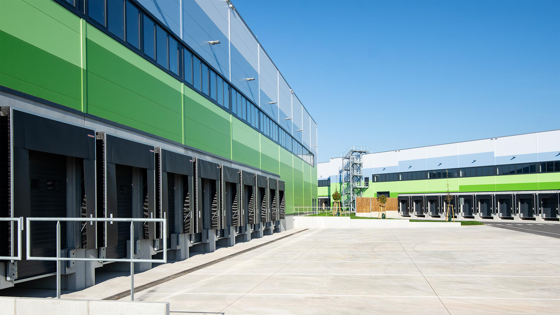 Moderne Lagerhalle mit grüner Fassade, Laderampen und klarem Himmel im Hintergrund.